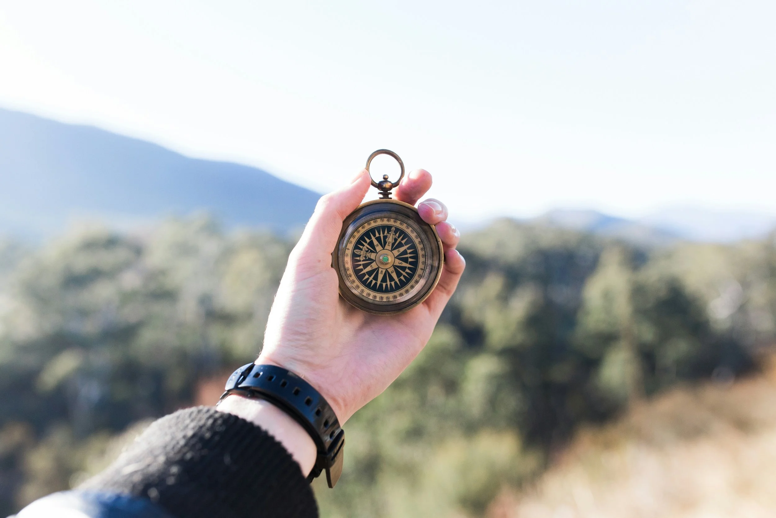 Picture of a compass being held in a woman's hand, held up in front of a blurred woodland scene. It depicts the leadership journey of The Empowered Leader.