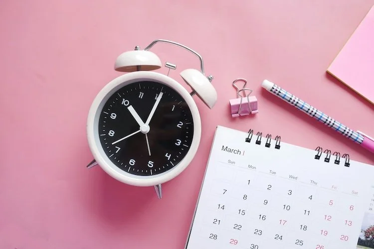 Picture of a clock and calendar on a pink desk to represent when everything is urgent.