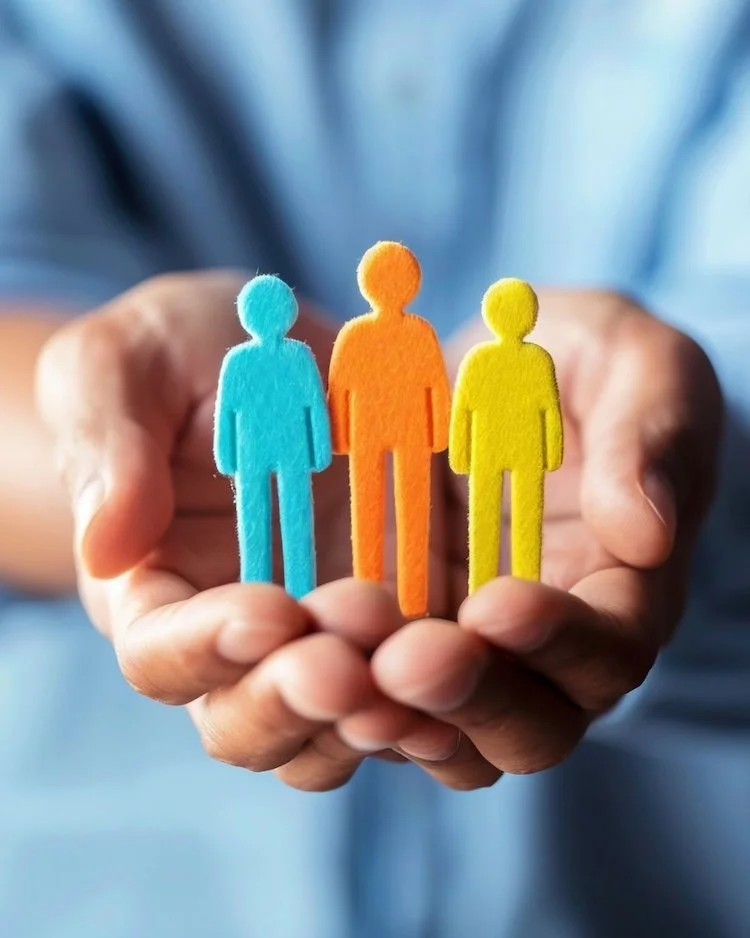 Male hands holding three felt figures in blue, orange and yellow in the palm of his hand to represent a respectful culture in the Not Winging It Leadership Club.