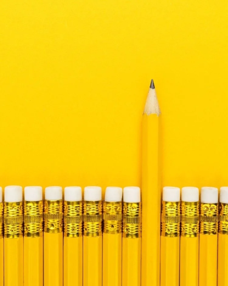 Yellow pencils in a row agains at yellow background with the eraser facing the top. A leaded end pencil is poling out, in the opposite direction.