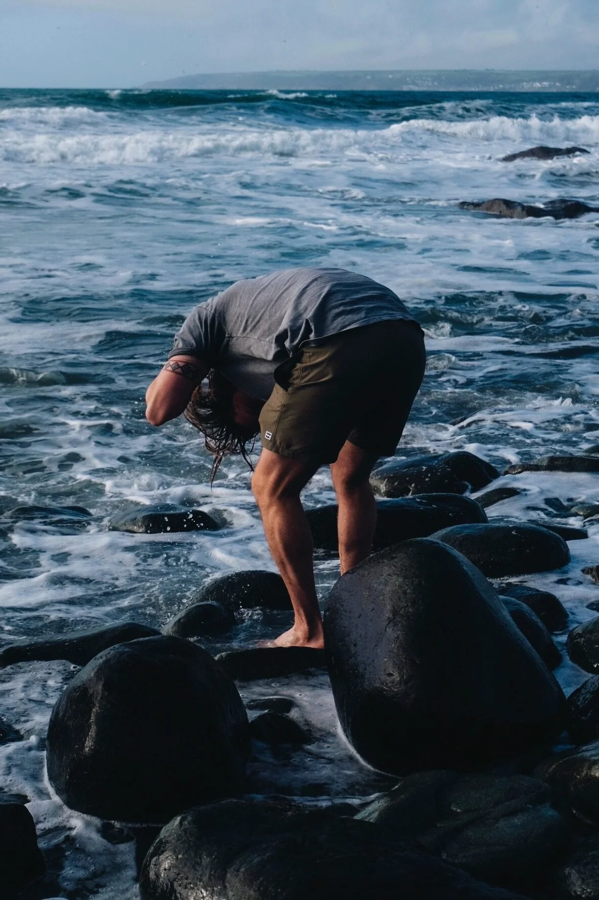 A man standing on wet boulders at the edge of the sea in Cornwall