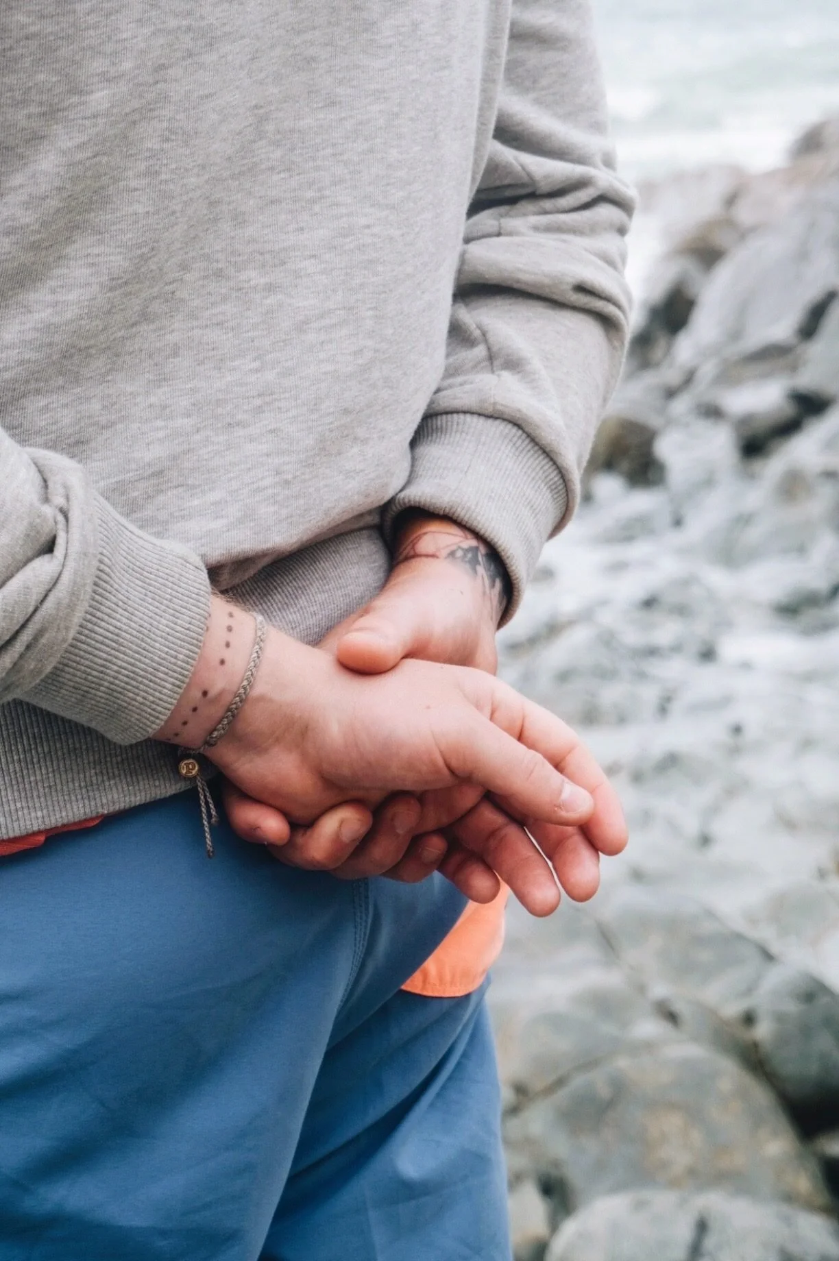 A man's hands clasped behind his back on a Cornish beach