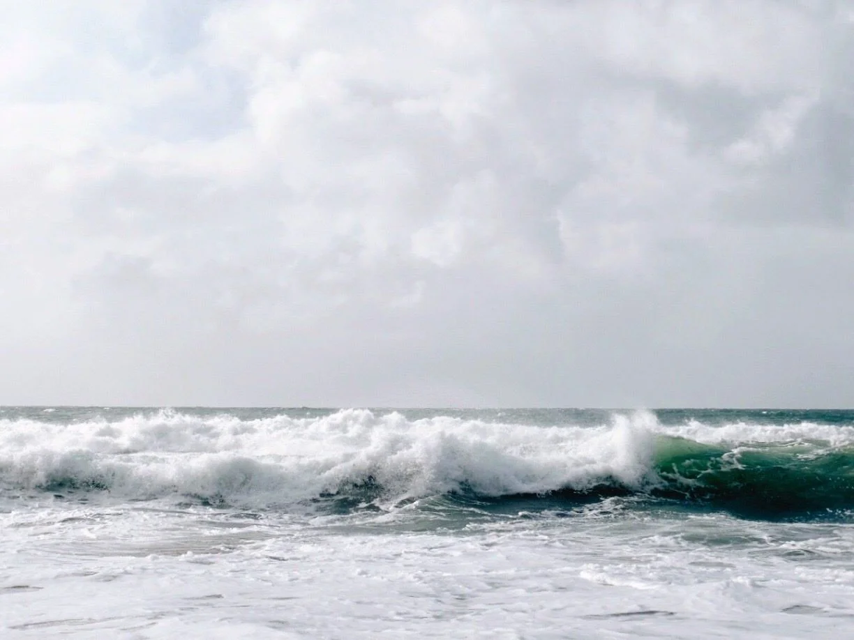 A wave breaking on a Cornish beach under a big sky