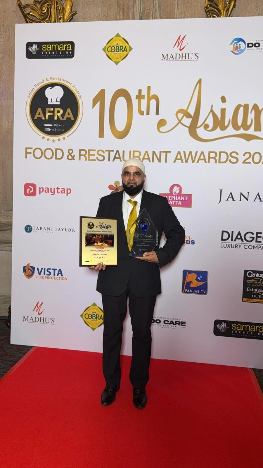 Man in a black suit and yellow tie holding an award and certificate at the 10th Asian Food & Restaurant Awards event.