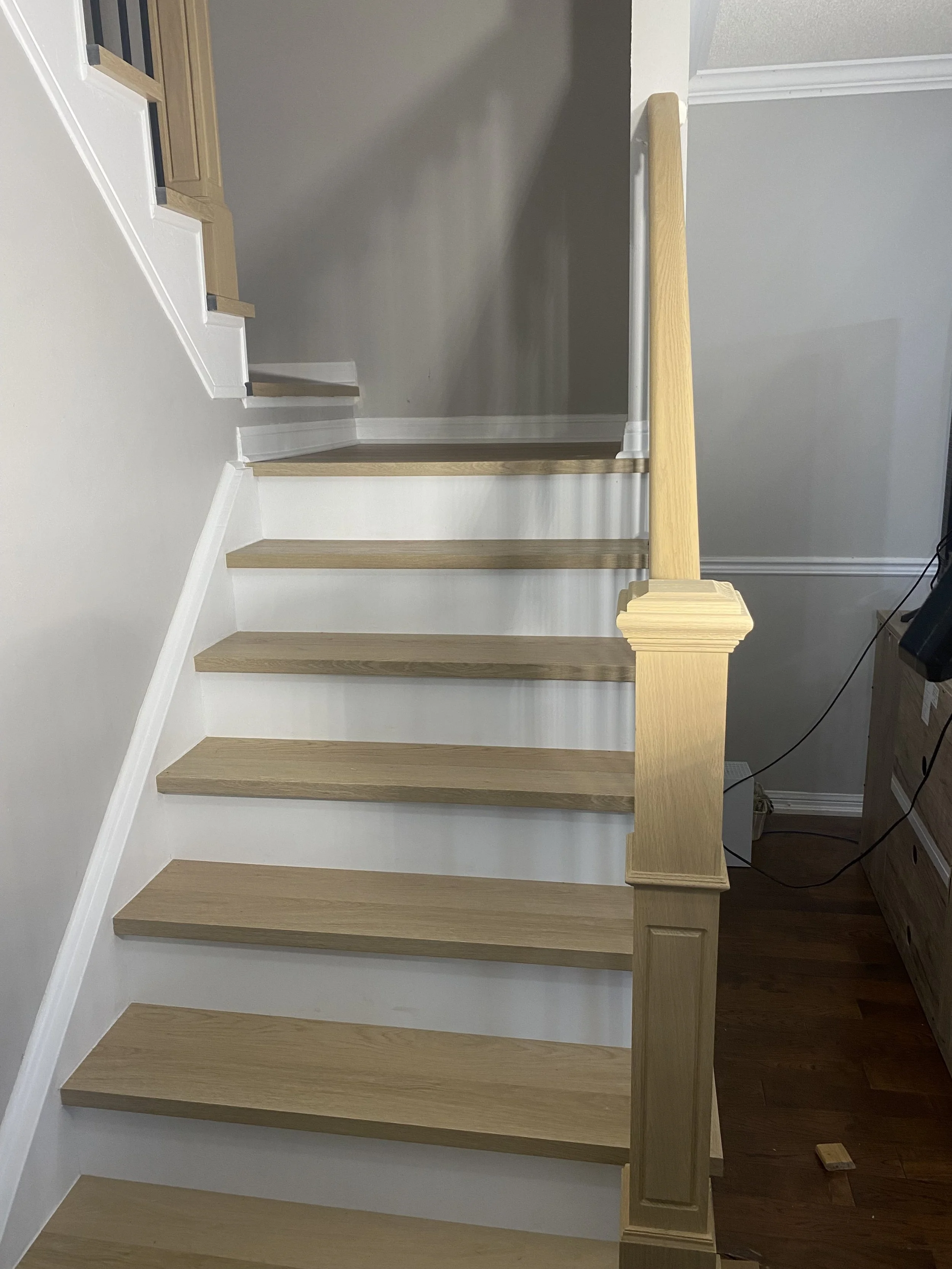 Interior staircase with light wood steps, white risers, and a light wood handrail and newel post.