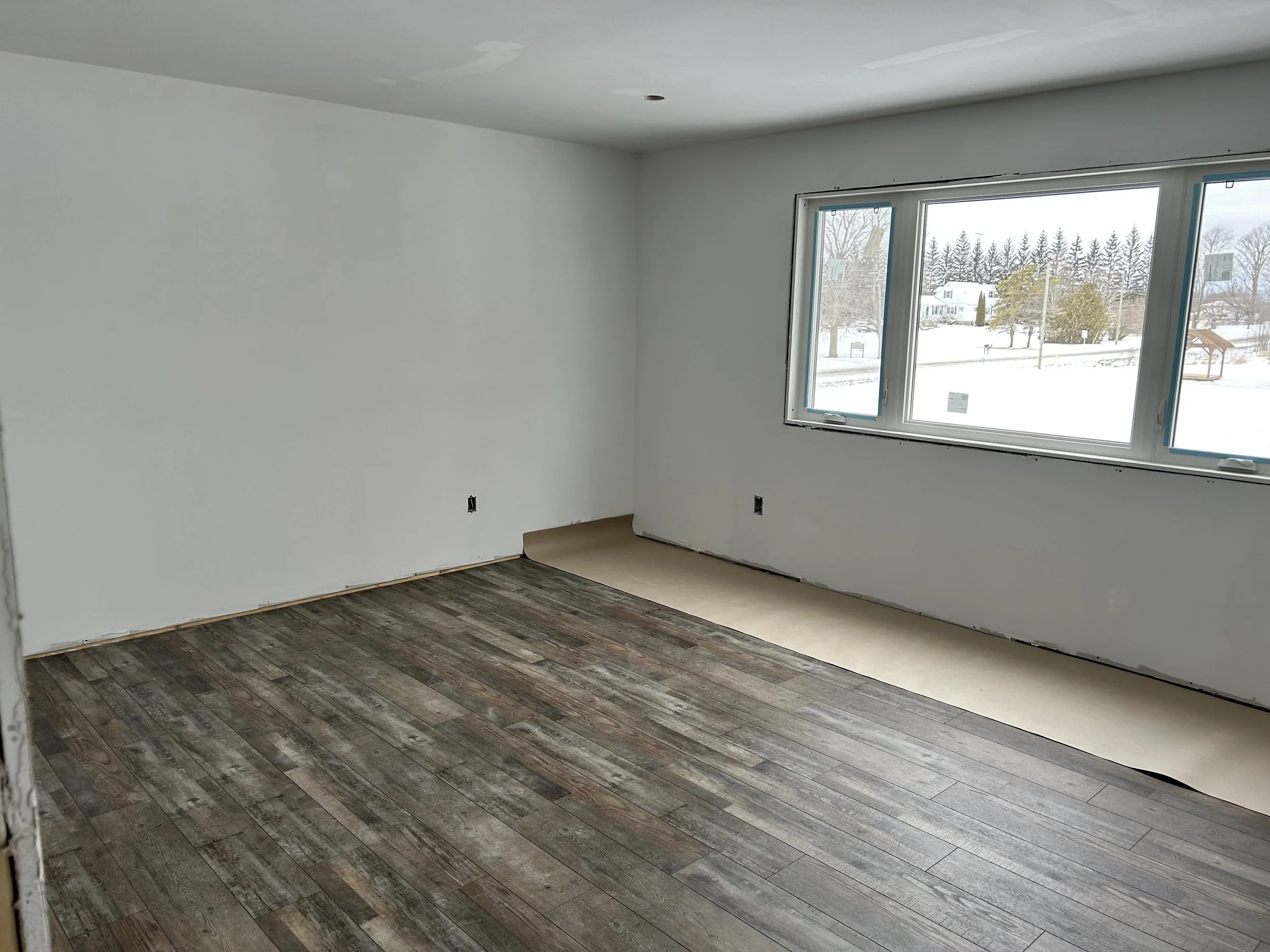 Unfinished room with white walls, large window, wood-look flooring, and no furniture.
