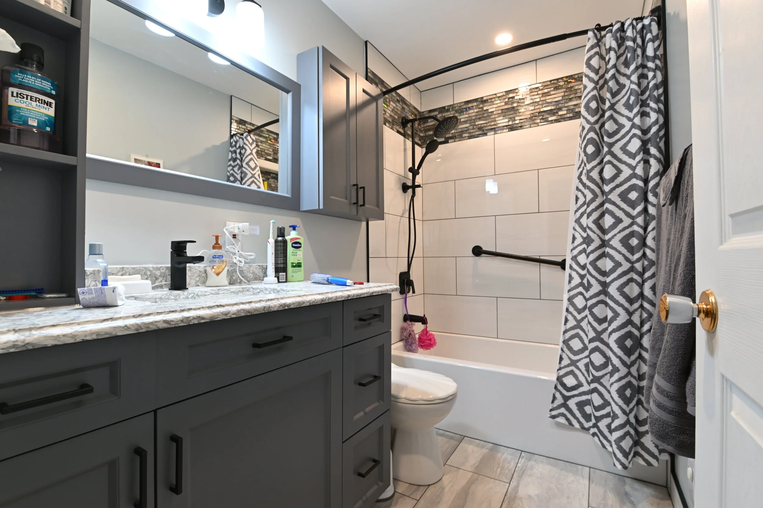Bathroom with gray cabinetry, marble countertop, large mirror, and a shower area with a curtain, grab bars, and a multi-head shower system.