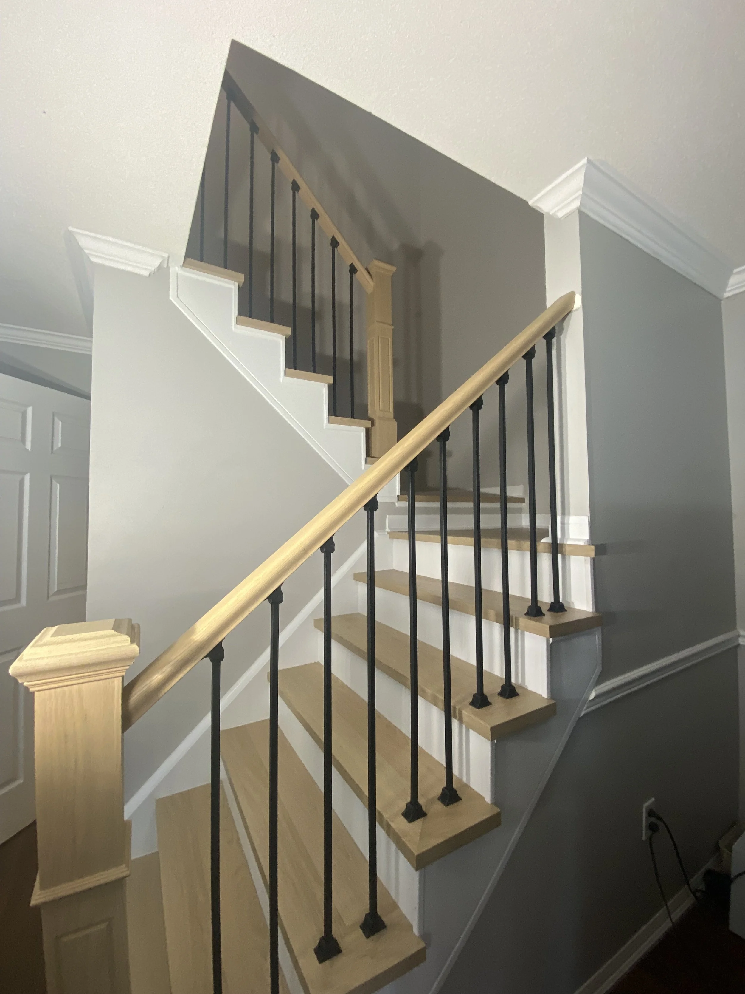 Staircase with wooden steps, black metal balusters, and wooden handrails, with a turn and upper landing area.