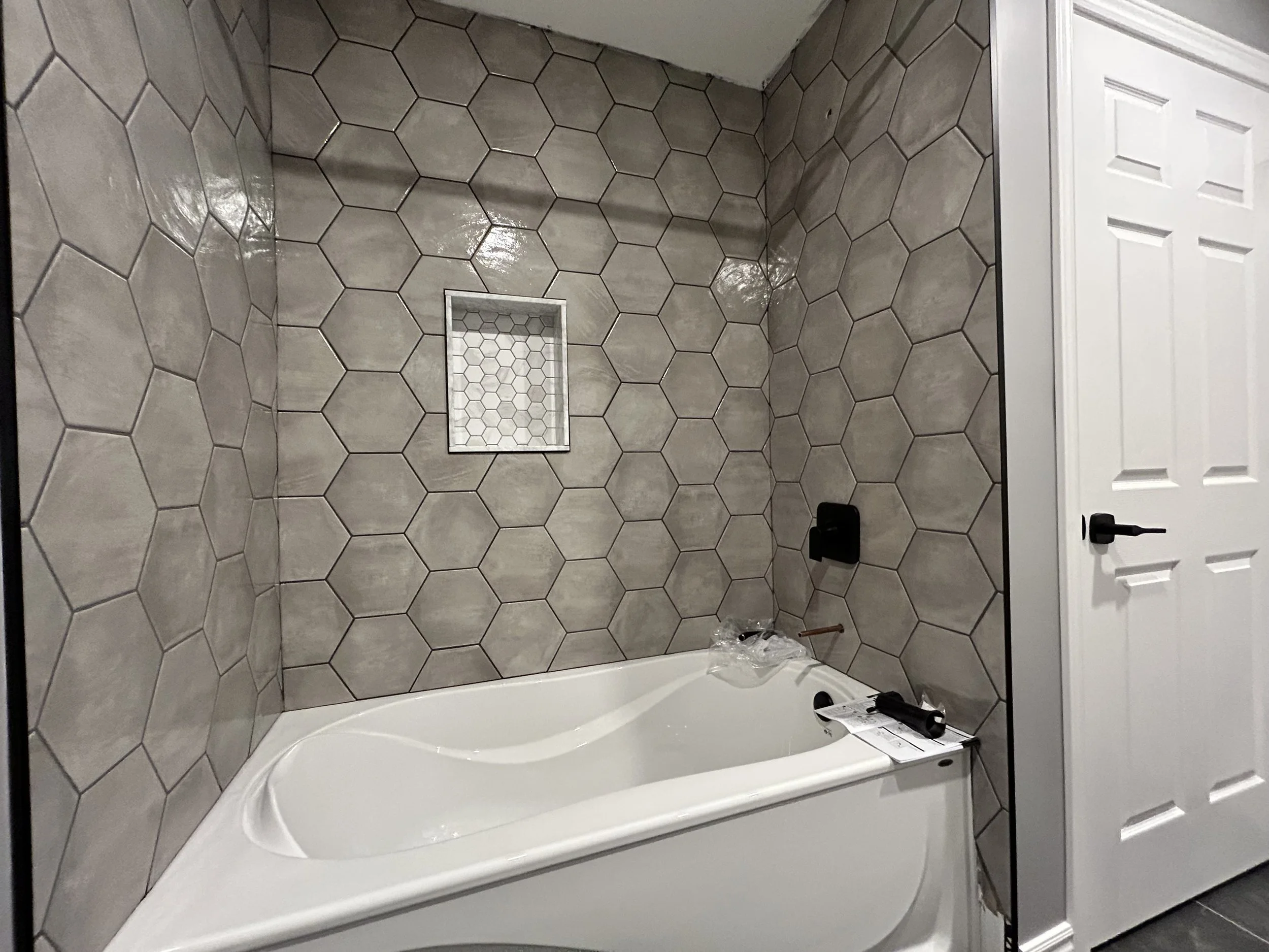 A new bathtub with a hexagon tile wall and built-in shower niche in a bathroom.