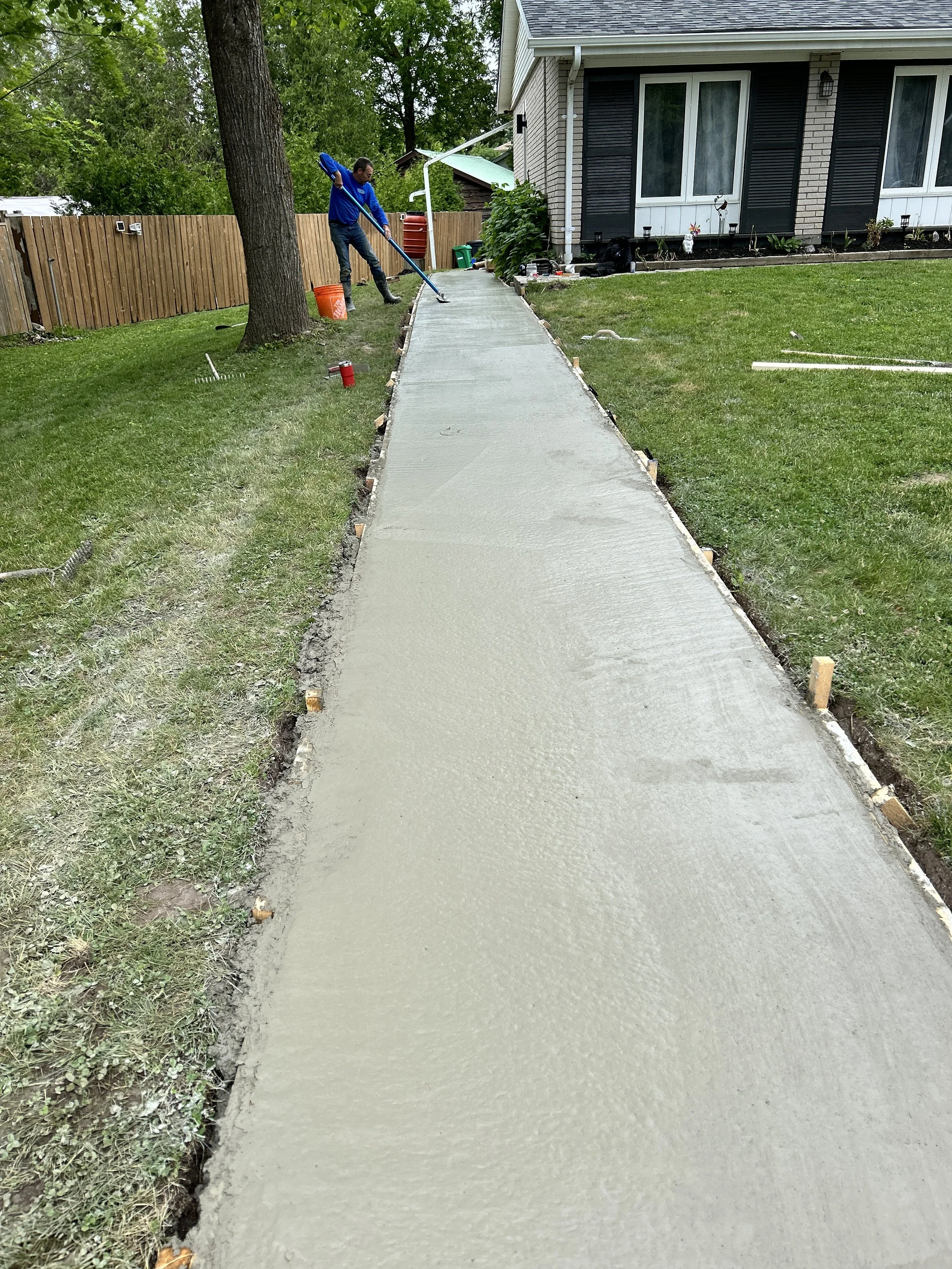 Person smoothing wet concrete on a sidewalk in a residential yard.
