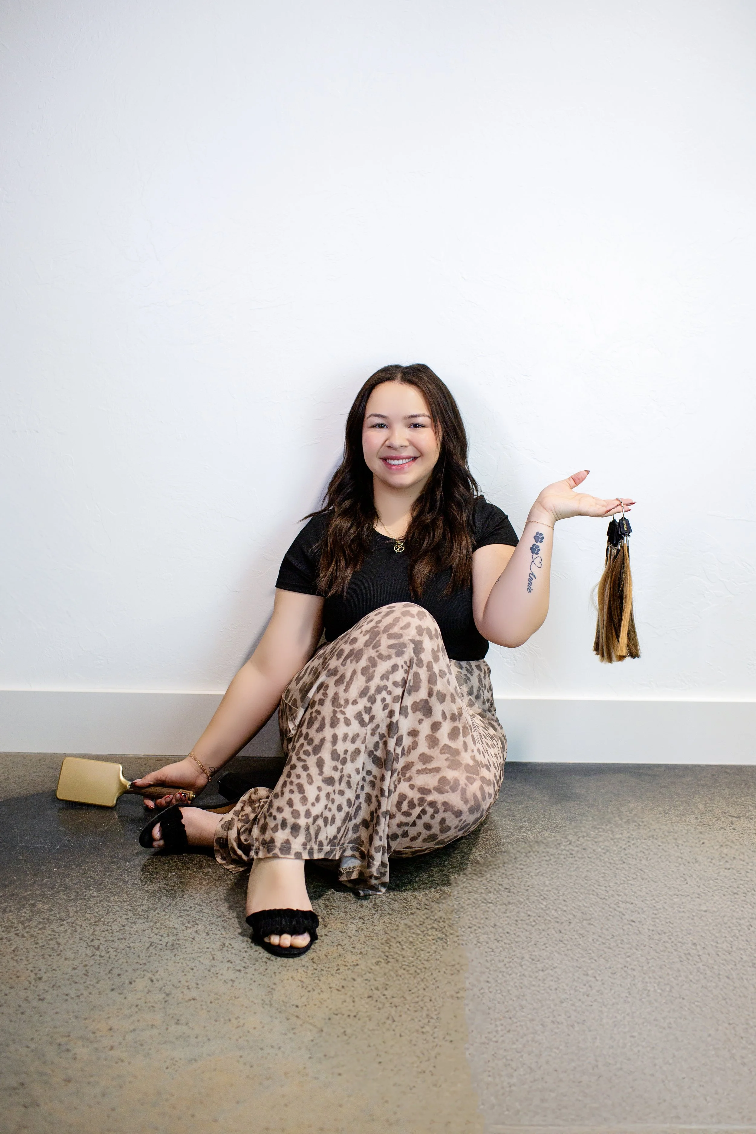 A woman sitting on the floor smiling while holding a graduation tassel.
