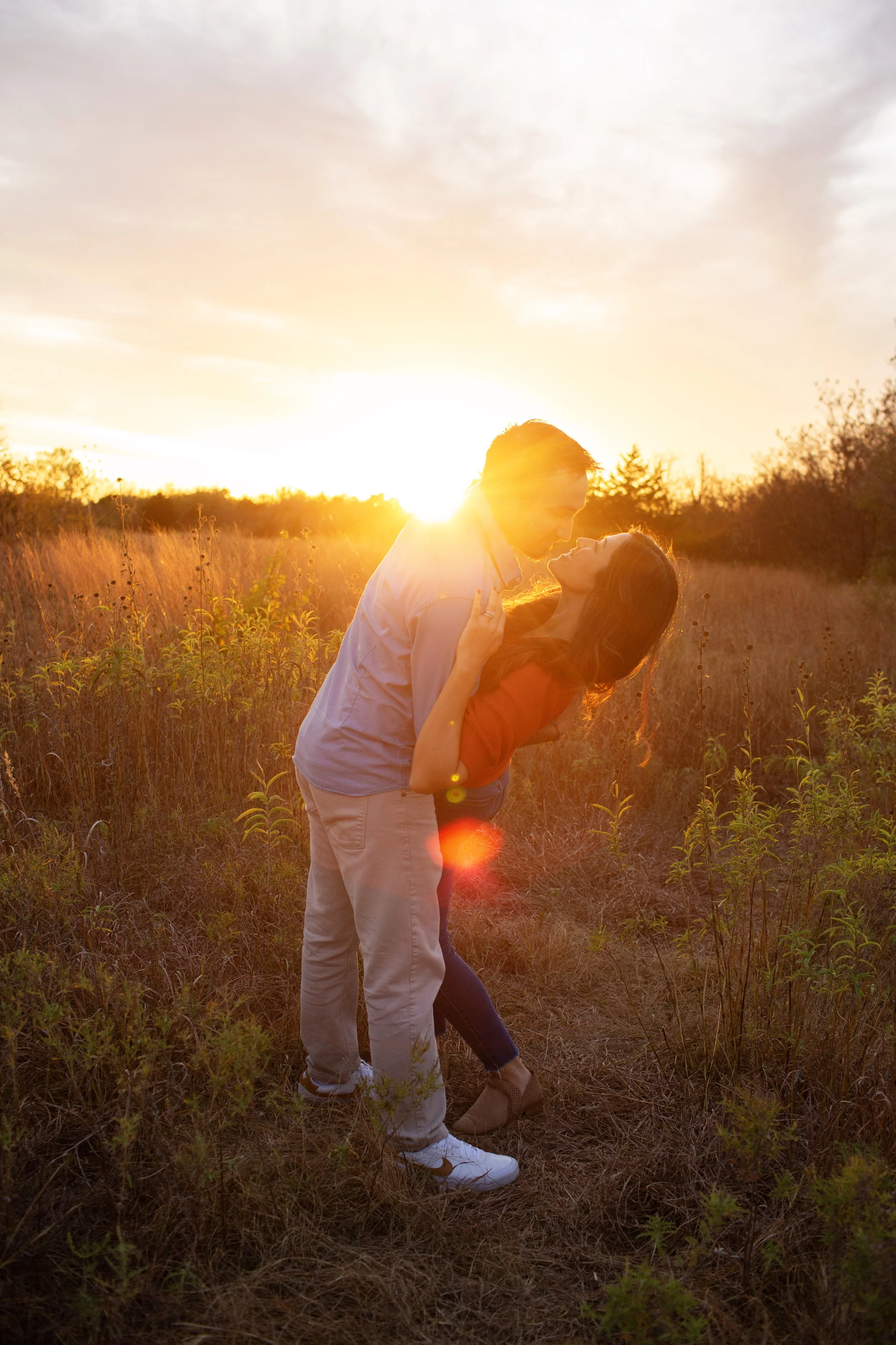 A couple is dancing in a field during sunset with the sun behind them.