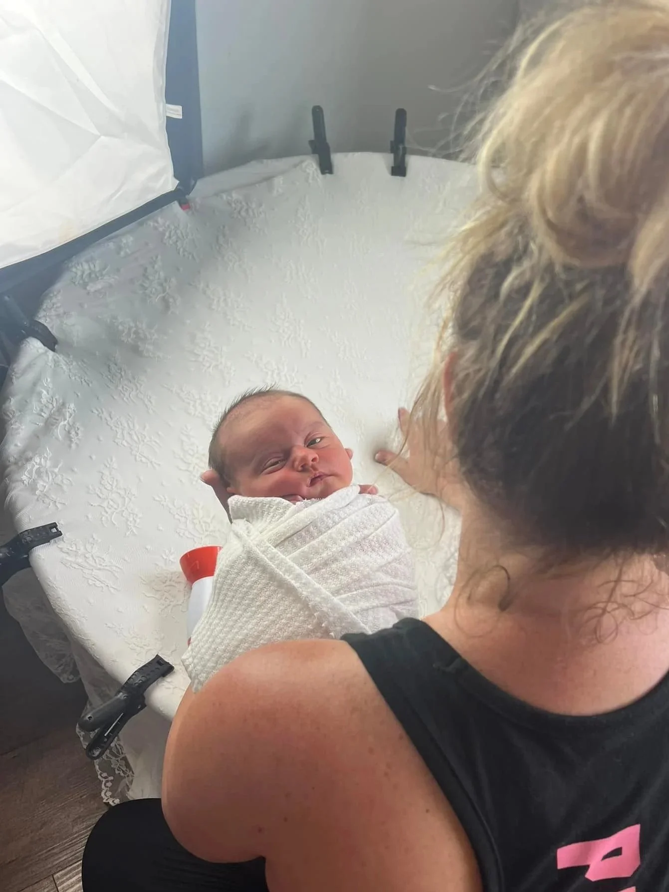 A newborn baby wrapped in a white blanket on a changing table, with an adult woman looking at the baby.