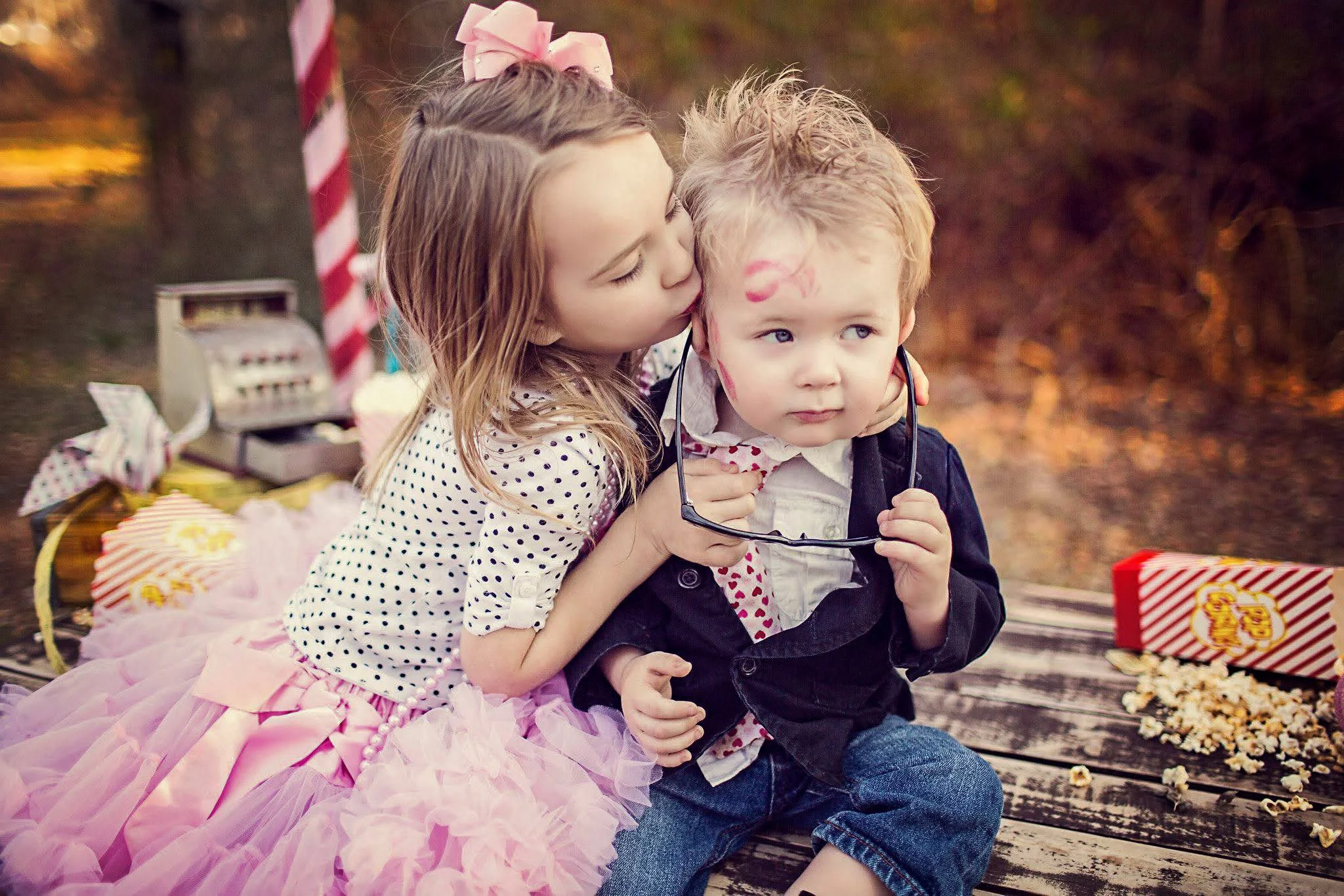 A young girl kisses a boy on the cheek at a picnic, with popcorn and snacks around them.
