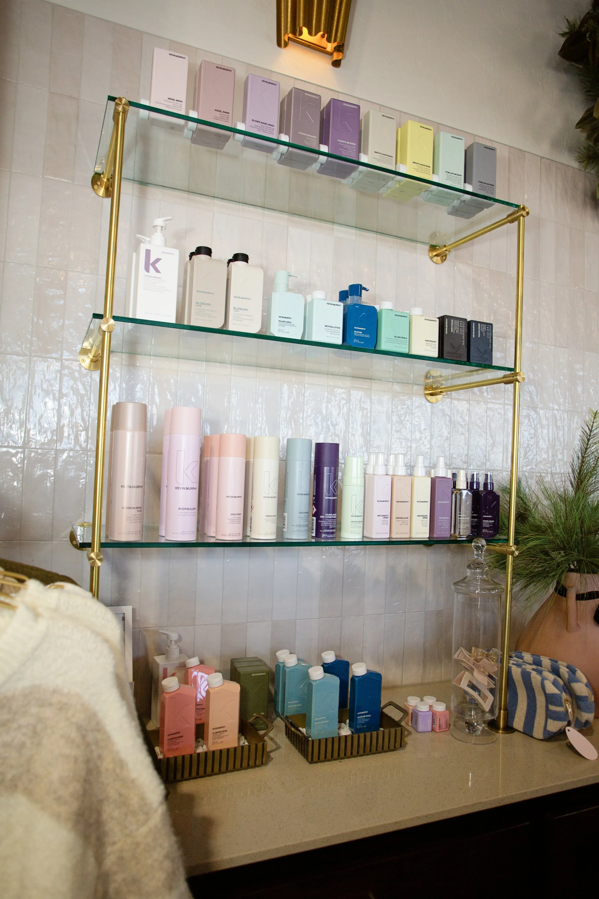 A display shelf with various colorful skincare and haircare products on glass shelves against a tiled wall.