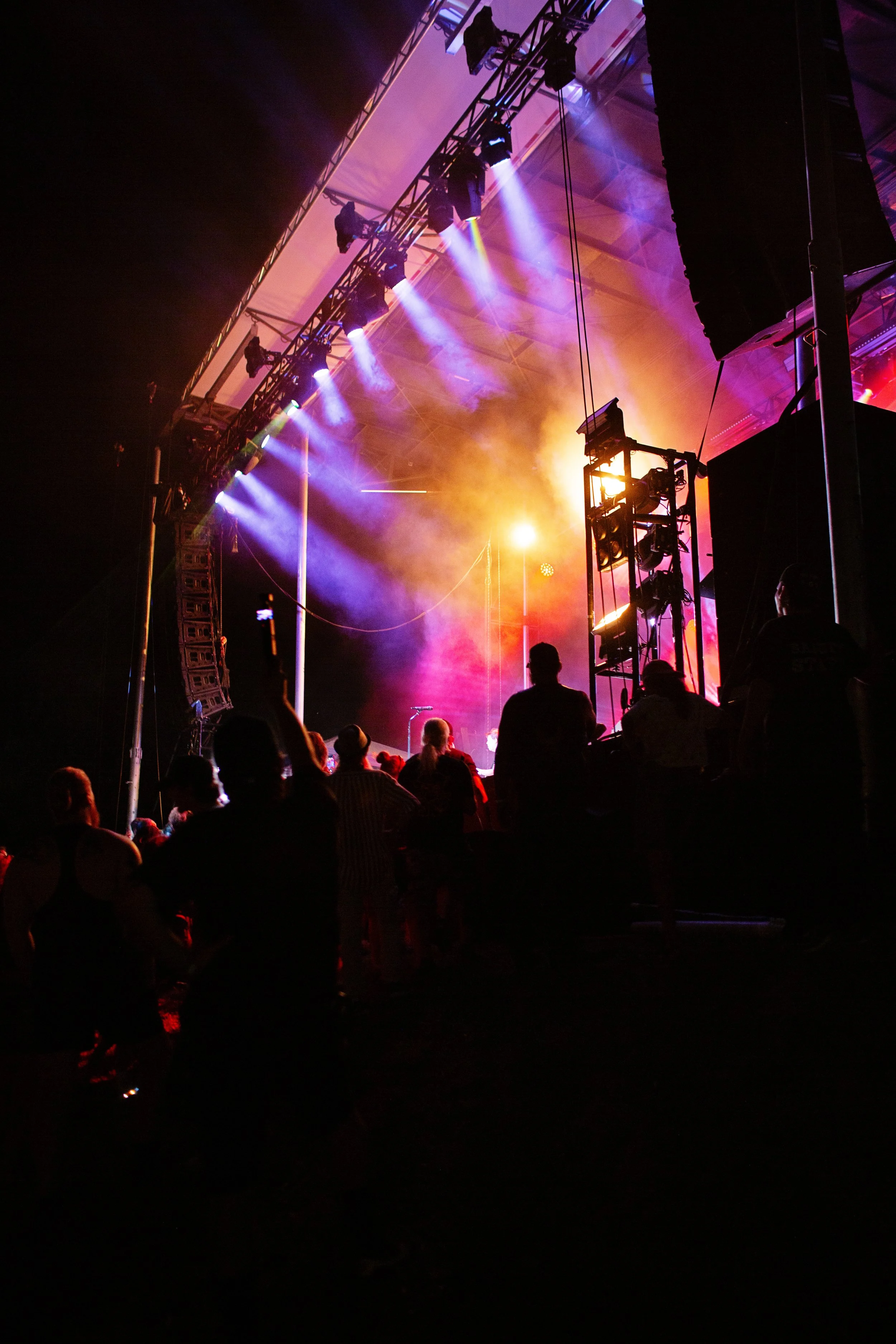 A concert stage with colorful lights and smoke, audience silhouettes, and sound equipment.