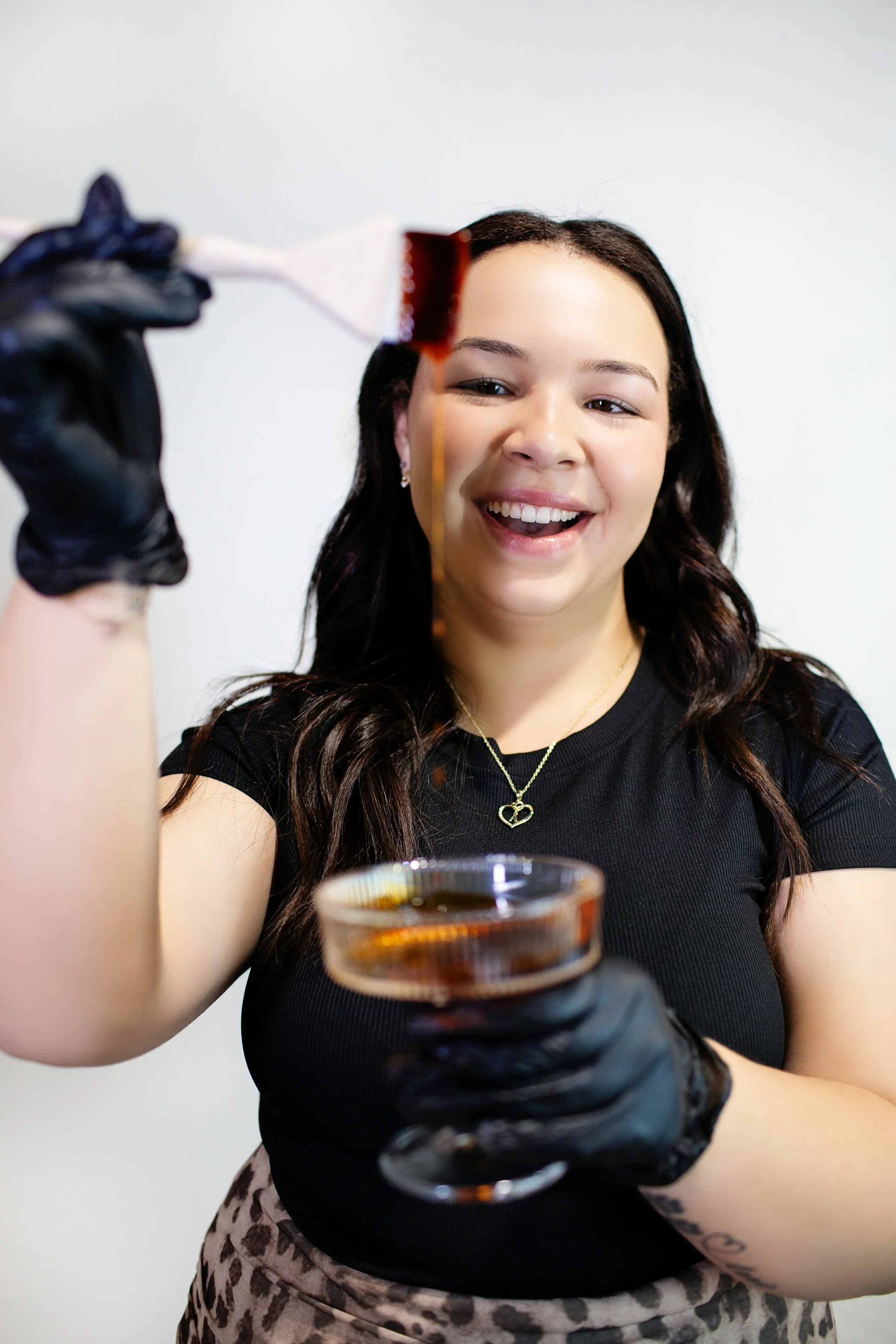 Woman smiling and pouring caramel on a spatula, wearing black gloves and holding a glass bowl of caramel