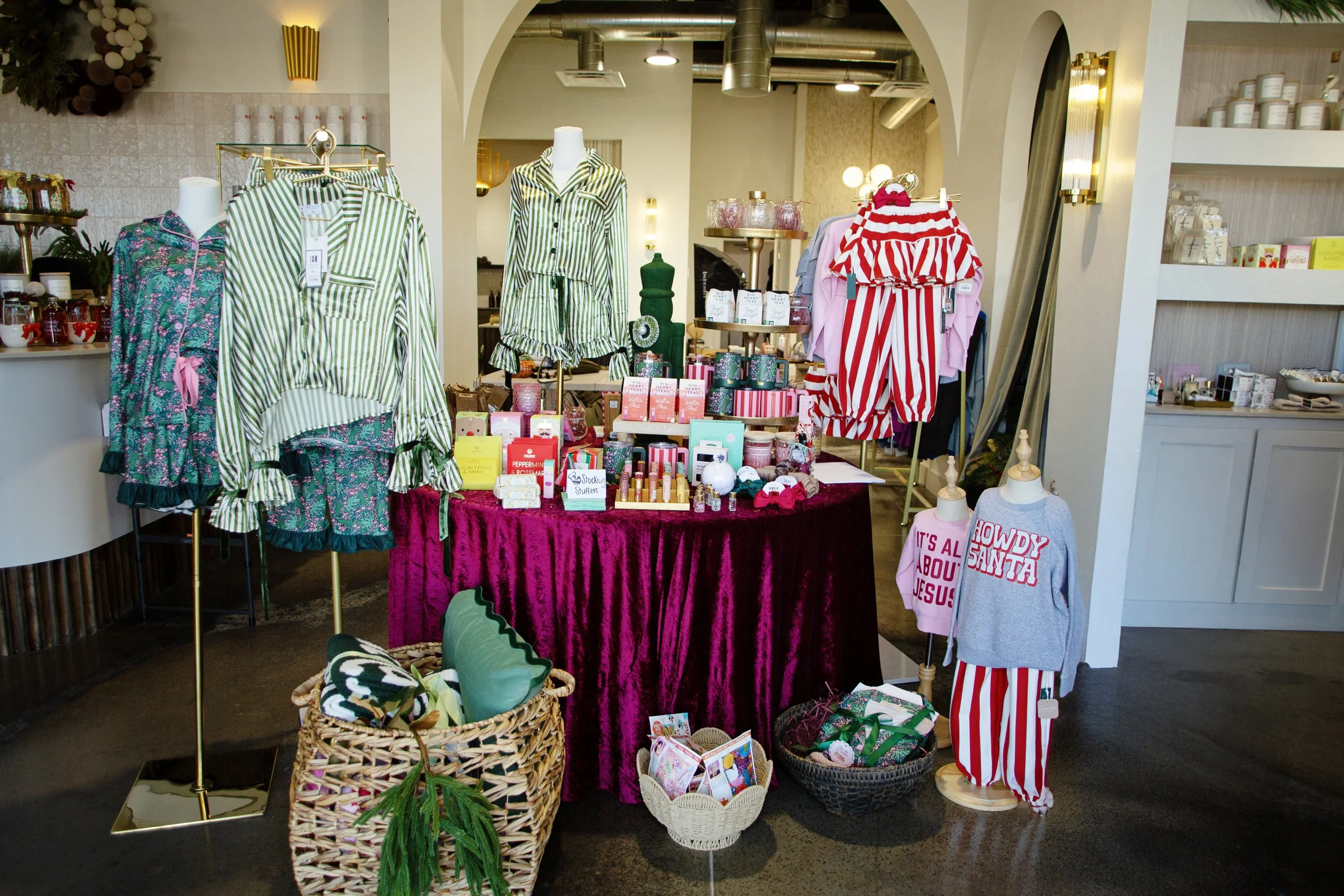 Display of holiday-themed pajamas, clothing, and gifts on a table and mannequins inside a retail store.