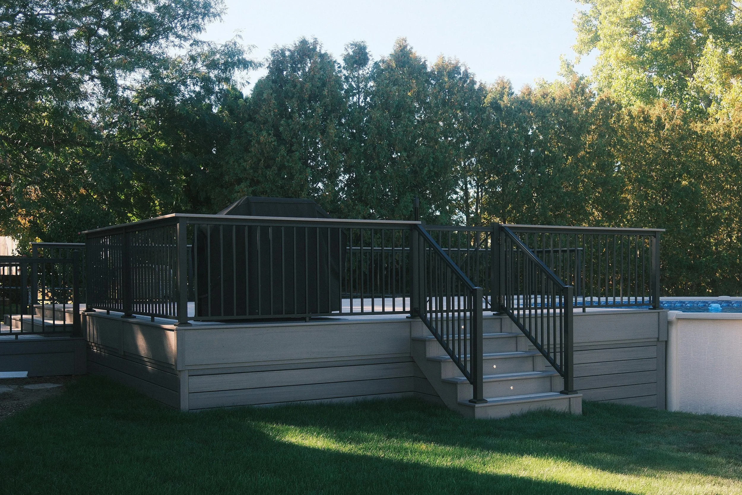 PVC above-ground pool deck with black railing and stairs.