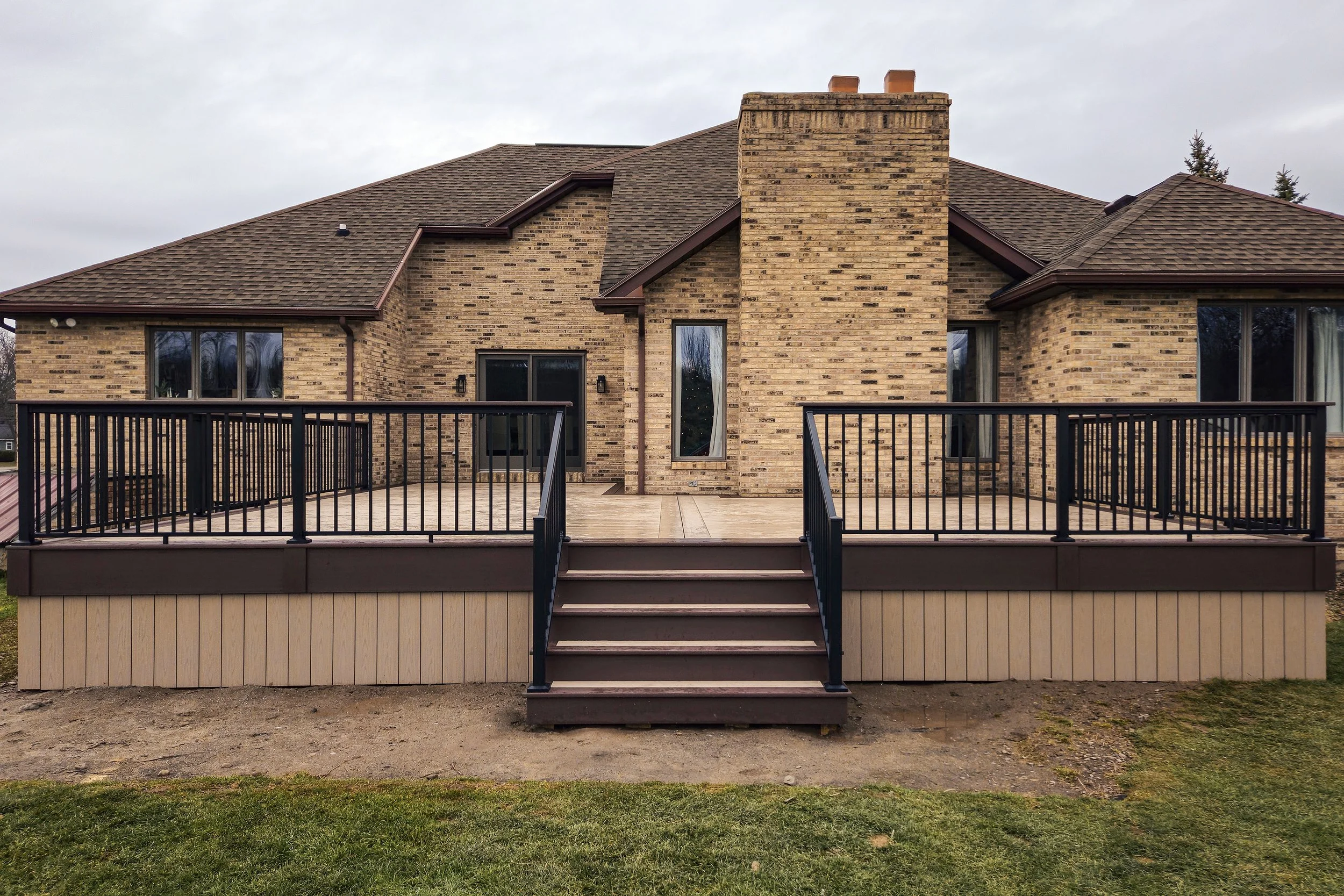 PVC deck with black railing and Brownstone skirting attached to brick home.