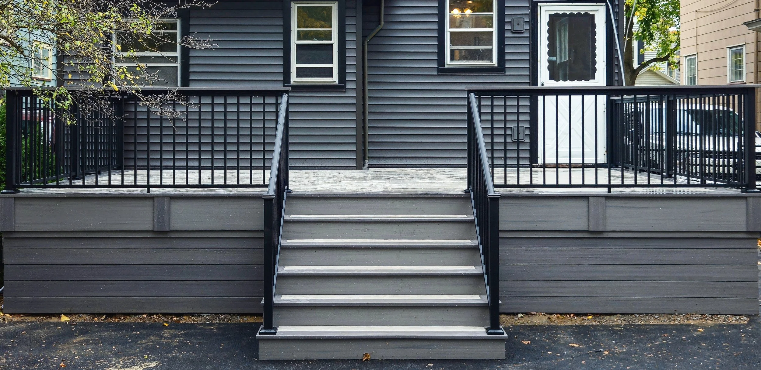 Gray PVC deck staircase with black railing in front of dark siding home.