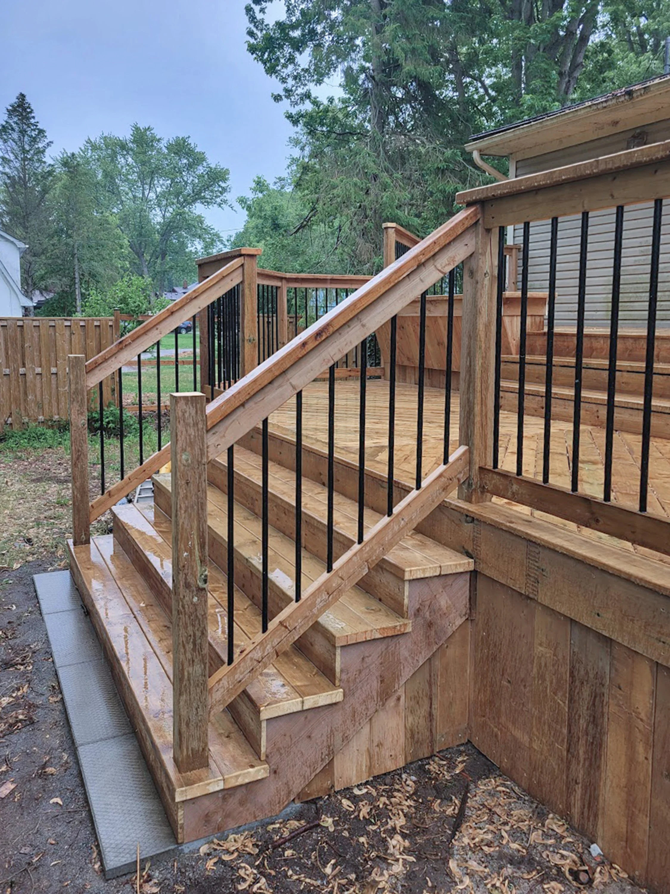 Wood deck staircase with black railing.