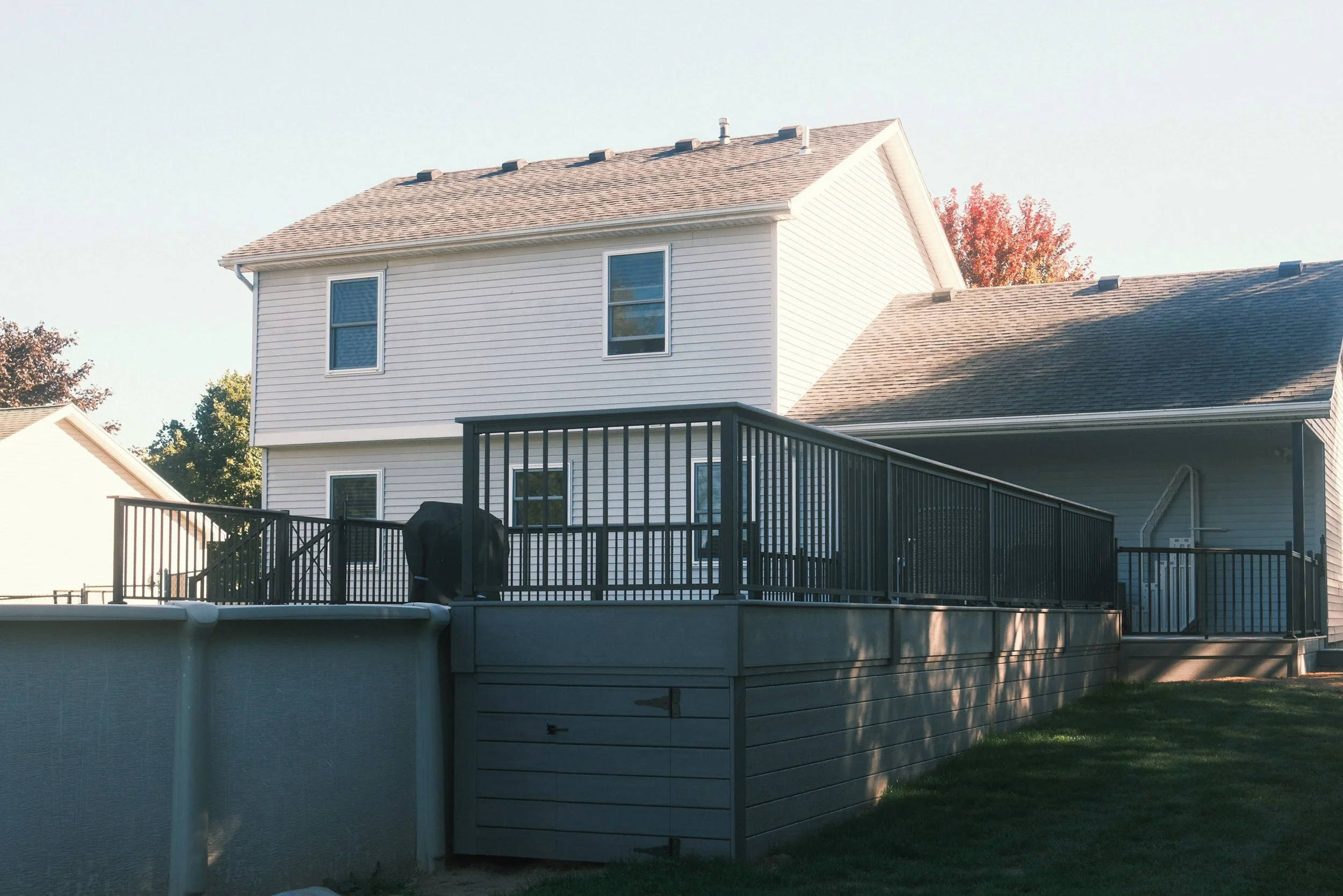 Raised backyard deck with railing attached to two-story home.
