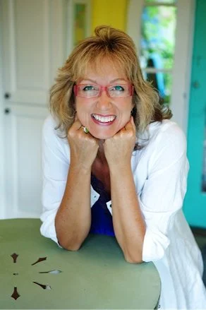 Woman in pink glasses sitting with elbows on table and smiling