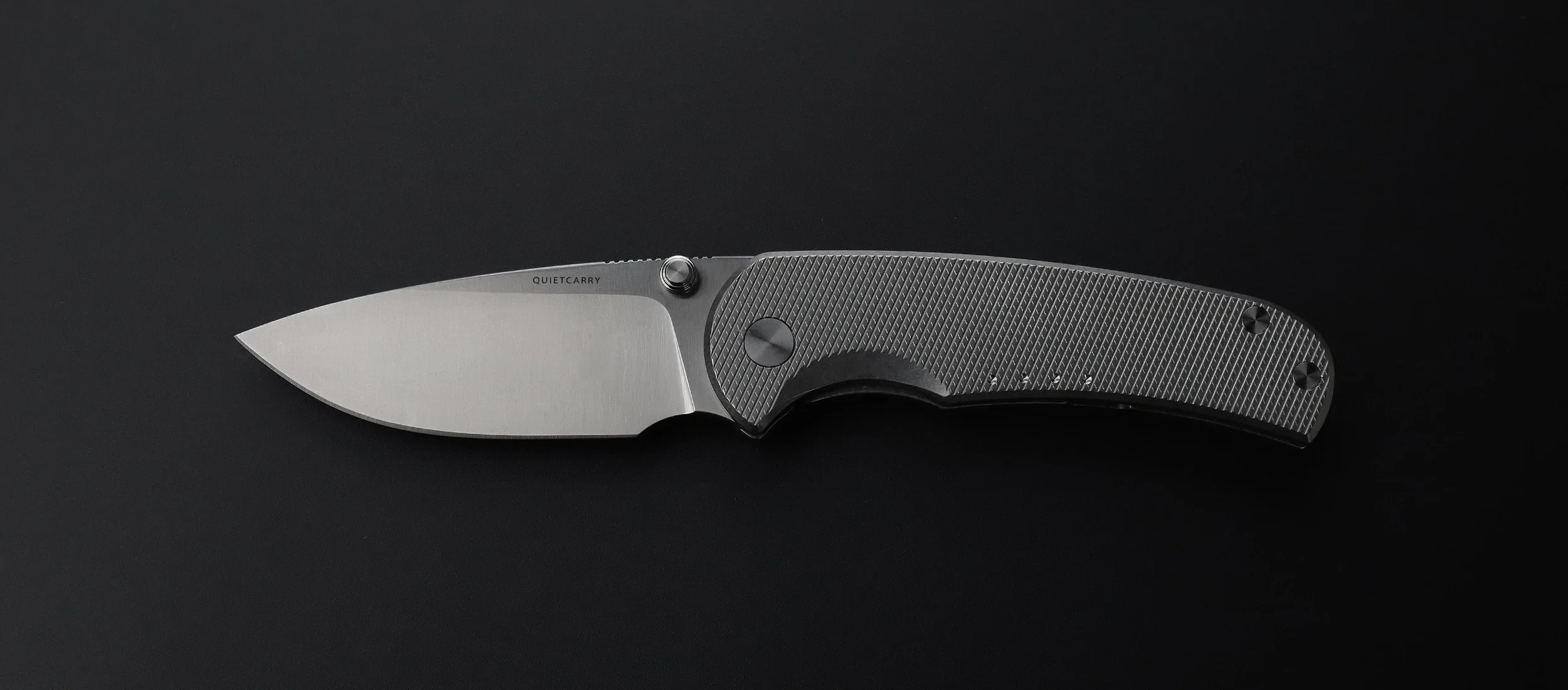A folding pocket knife with a silver blade and textured gray handle, positioned horizontally against a black background.