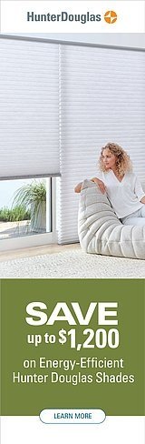 Woman sitting on a white couch in a living room with large horizontal Hunter Douglas window shades, promoting savings on energy-efficient window coverings.