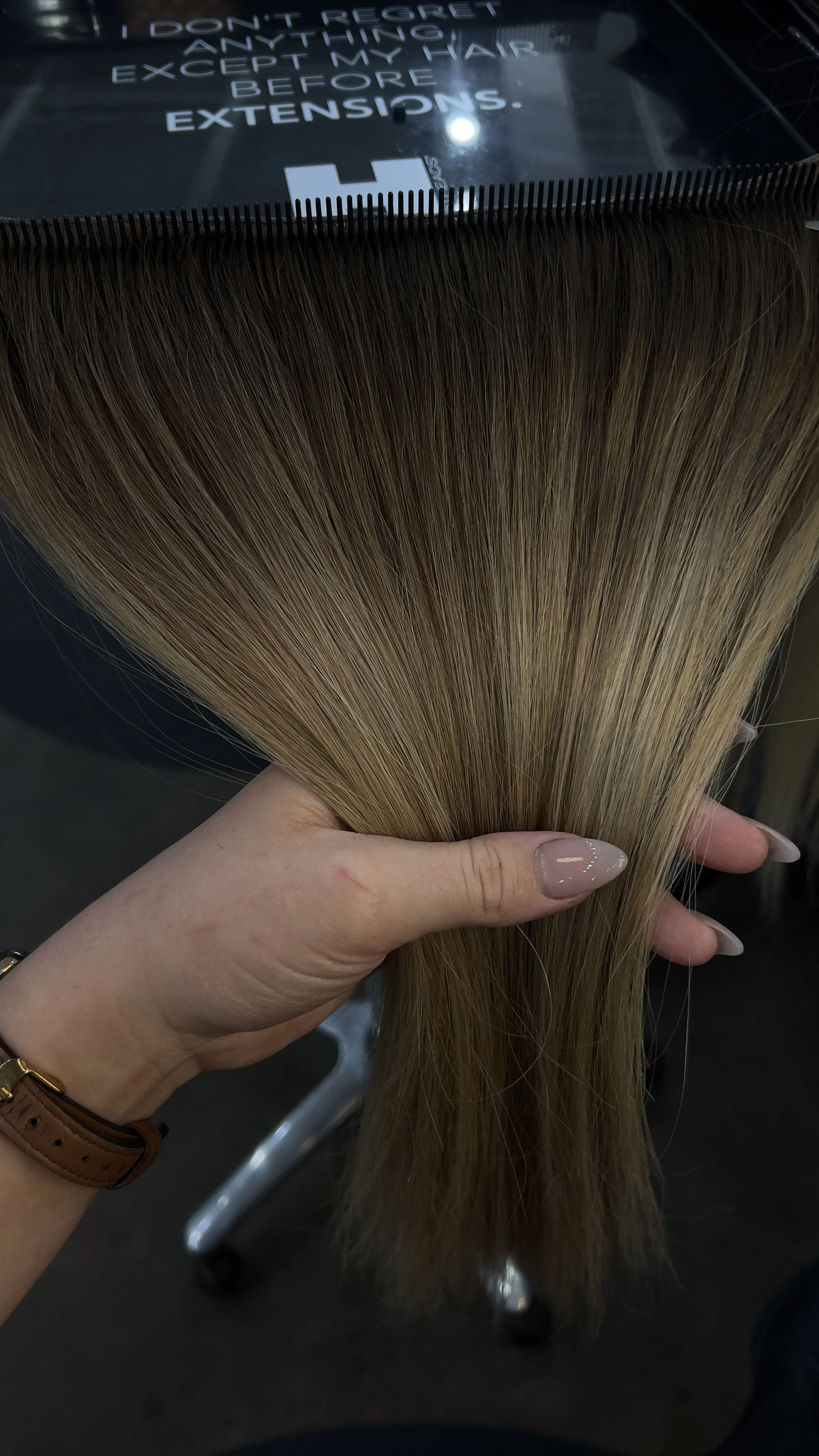 Someone holding a bundle of blonde hair extensions with a sign in the background that says, "I don't regret anything except my hair before extensions."