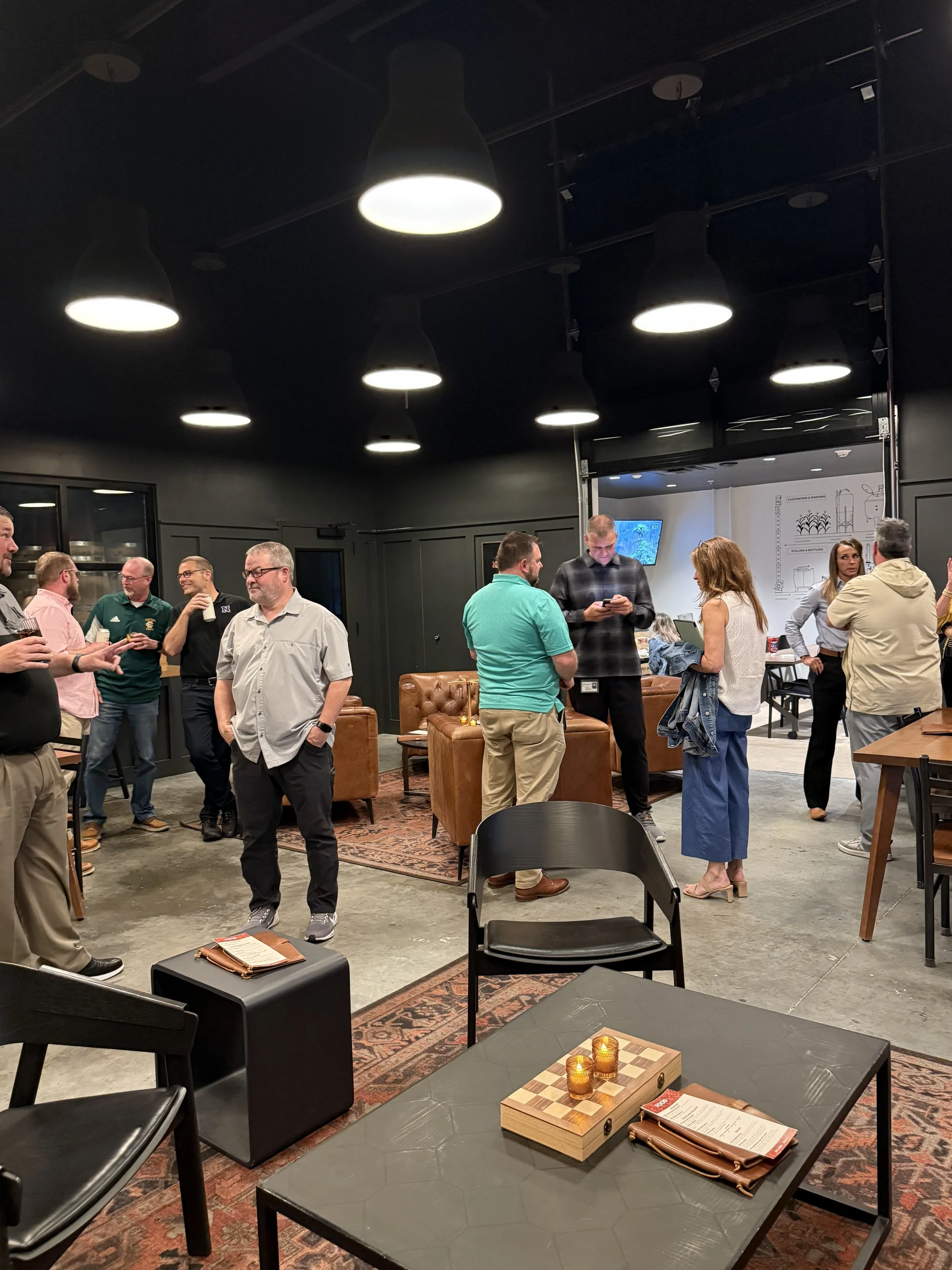 People socializing in a modern, dimly lit lounge or event space with black walls, hanging lights, and contemporary furniture.