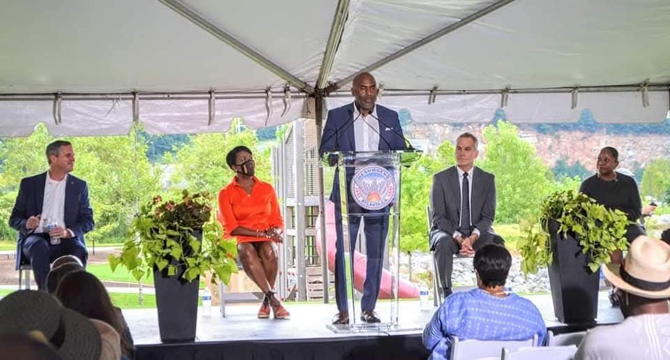 TJ Austin, Founder of Austin Advisory Group, speaking at a podium under a tent with several people seated behind him.