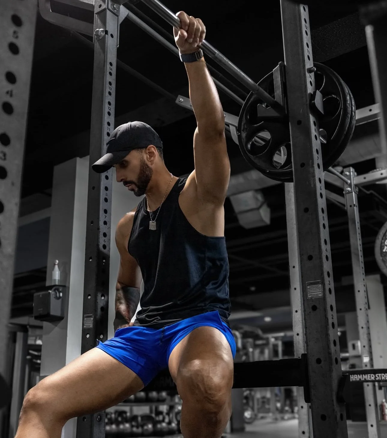 A man lifting a barbell while seated on a bench in a gym.