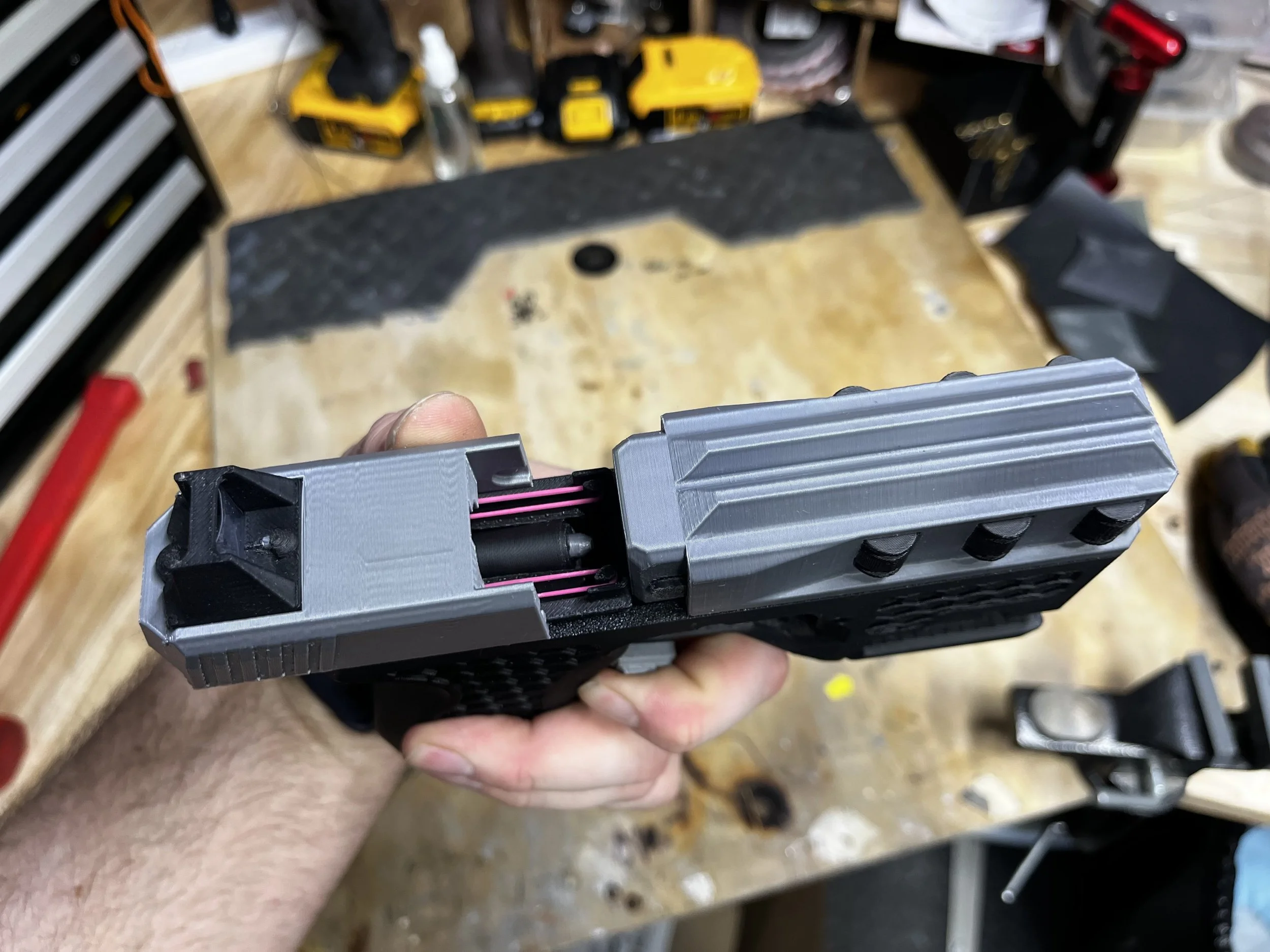Close-up of a prop coilgun slide being held in someone's hand in a workshop with tools and workbench in the background.