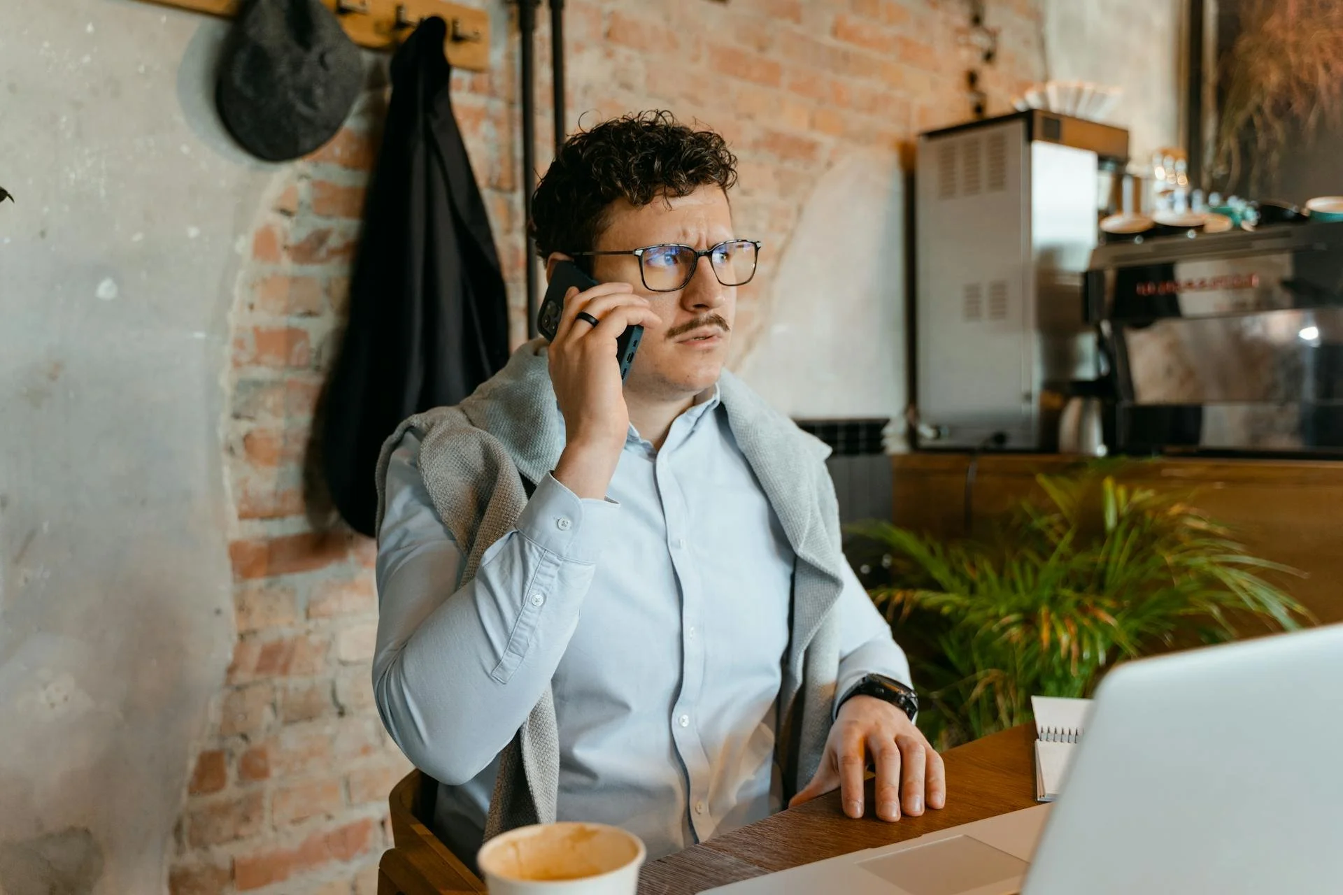 Man looking irritated while talking on the phone and working from home at a laptop