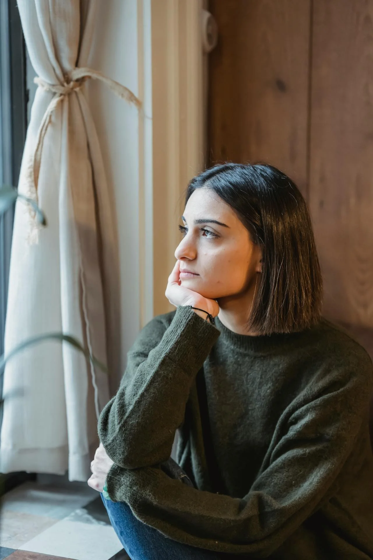 Woman seated near a window with a reflective posture, representing professional trauma counselling available in Alberta.