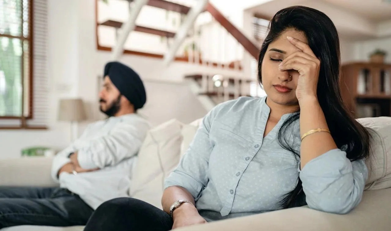 Couple sitting apart on a couch in a home setting, representing relationship counselling services in Alberta.