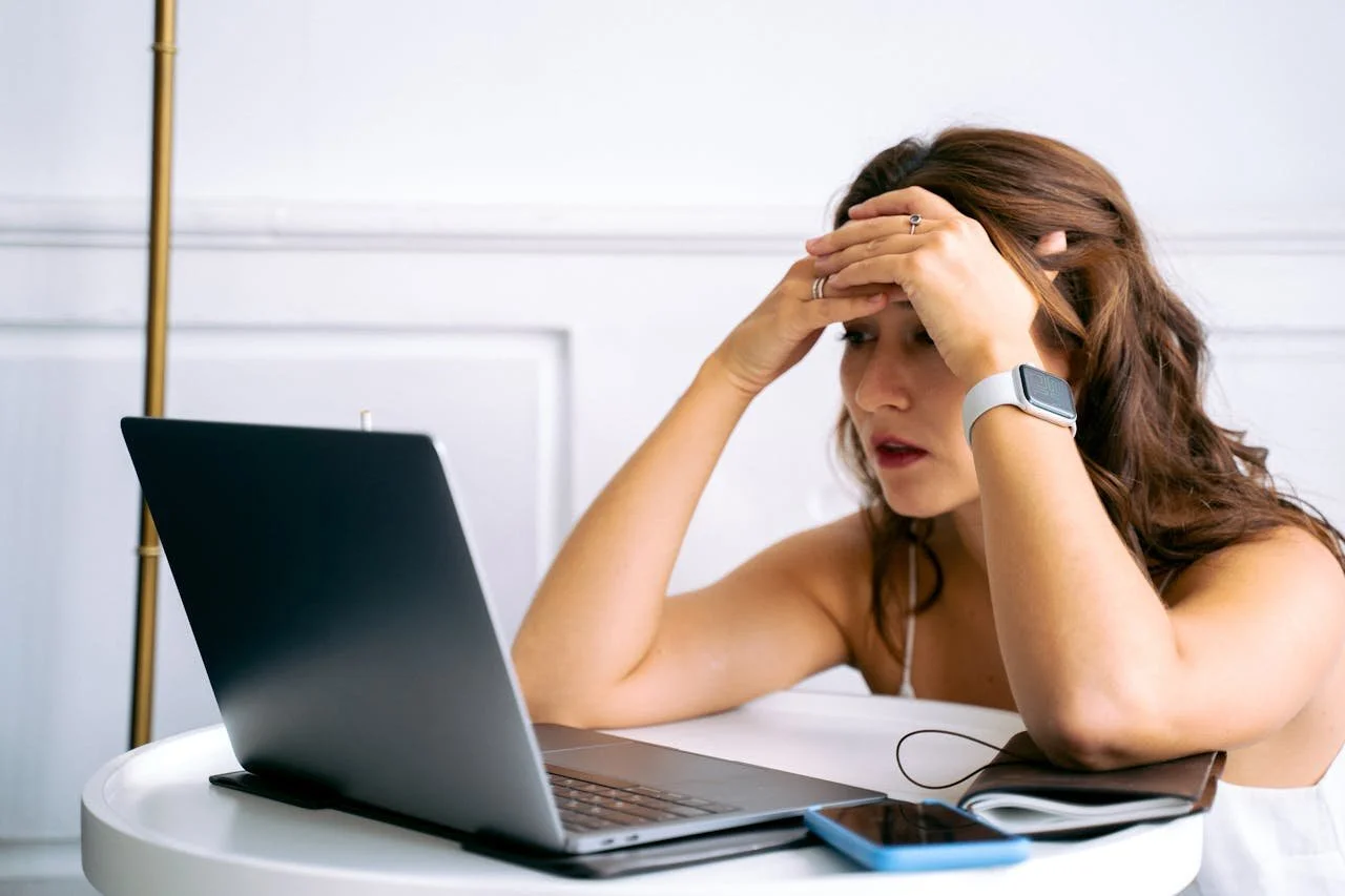 Woman looking overwhelmed while working on a laptop during a stressful workday at home