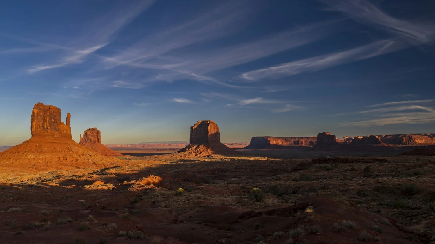 Sandstone buttes in Monument Valley at sunset under a sky streaked with thin clouds