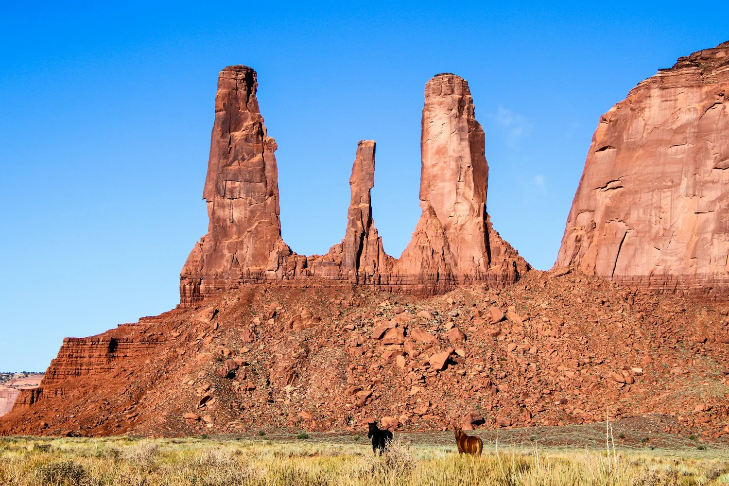 Three sandstone spires rising over open desert in Monument Valley under a clear blue sky