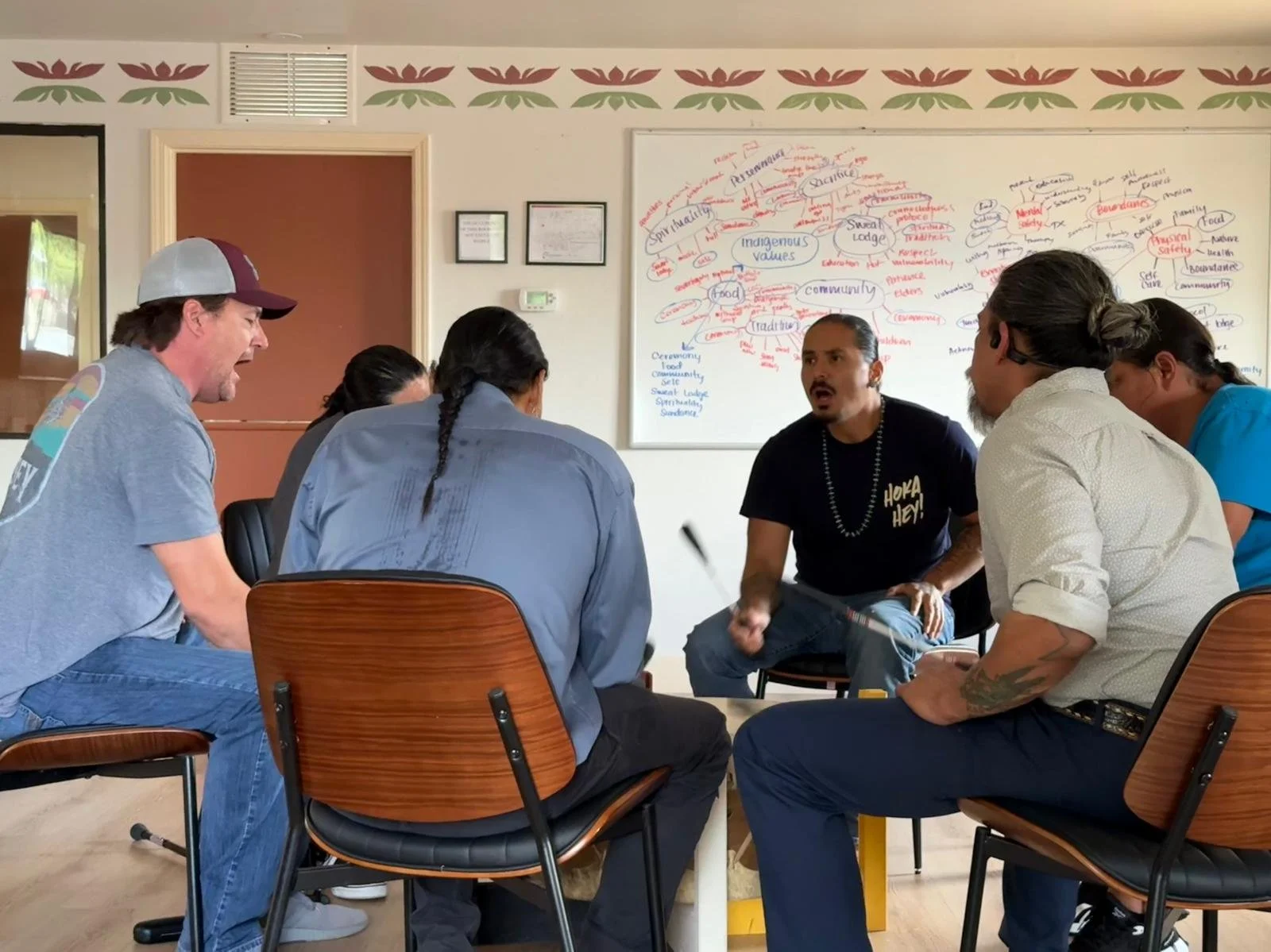 Group of seven people standing in an indoor room, smiling and posing for a photo, with a colorful protest art painting on the wall behind them.