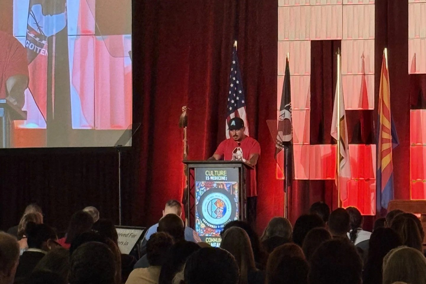 Che Jim speaking in front of a large auditorium of people at the NIHB National Indian Health Conference about Missing and Murdered Indigenous Women and People in Gila River, Arizona.