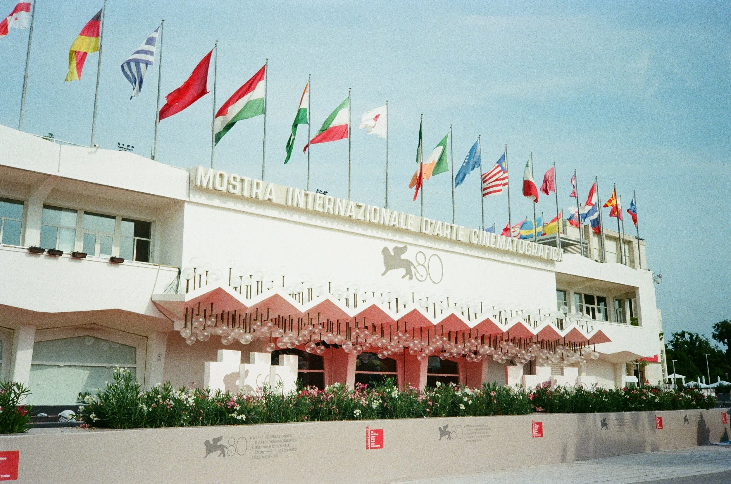 Edificio bianco con bandiere di vari paesi sulla terrazza e l'insegna 'Mostra Internazionale d'Arte Cinematografica' a Venezia