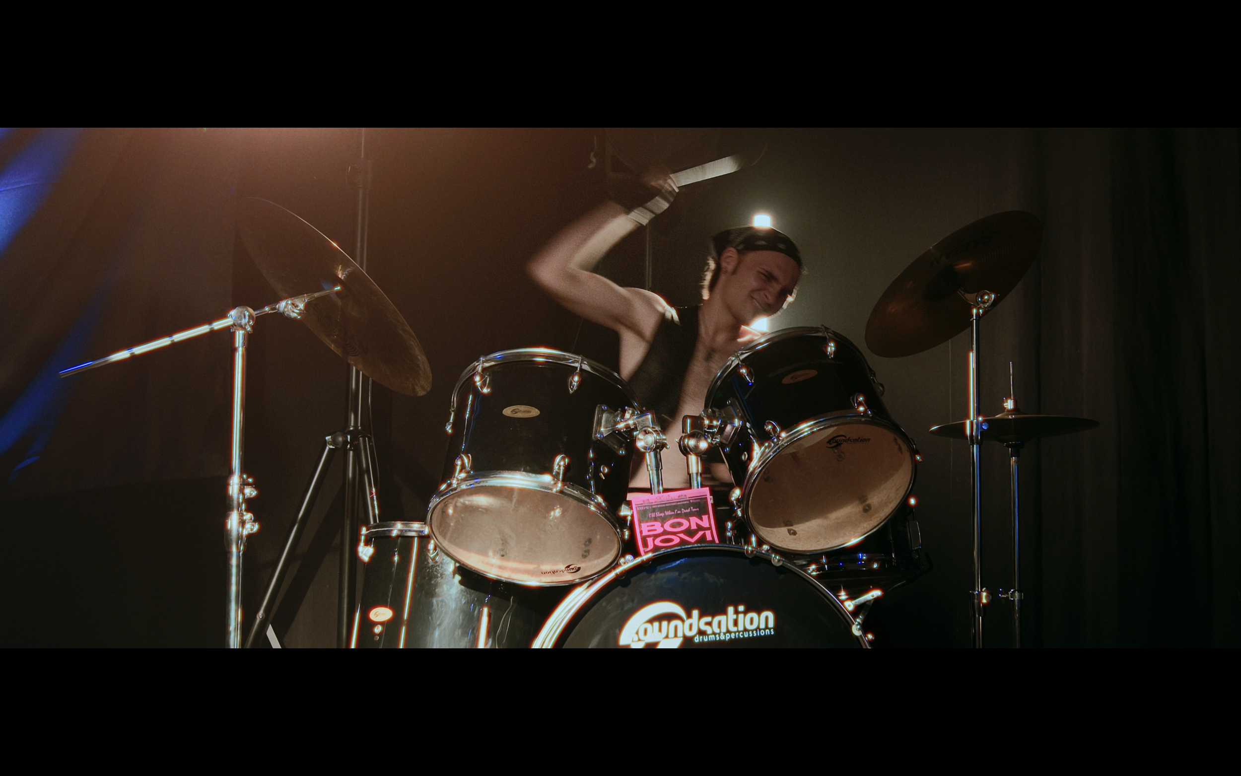 Una persona che suona la batteria durante un concerto, con musica e luci sul palco.