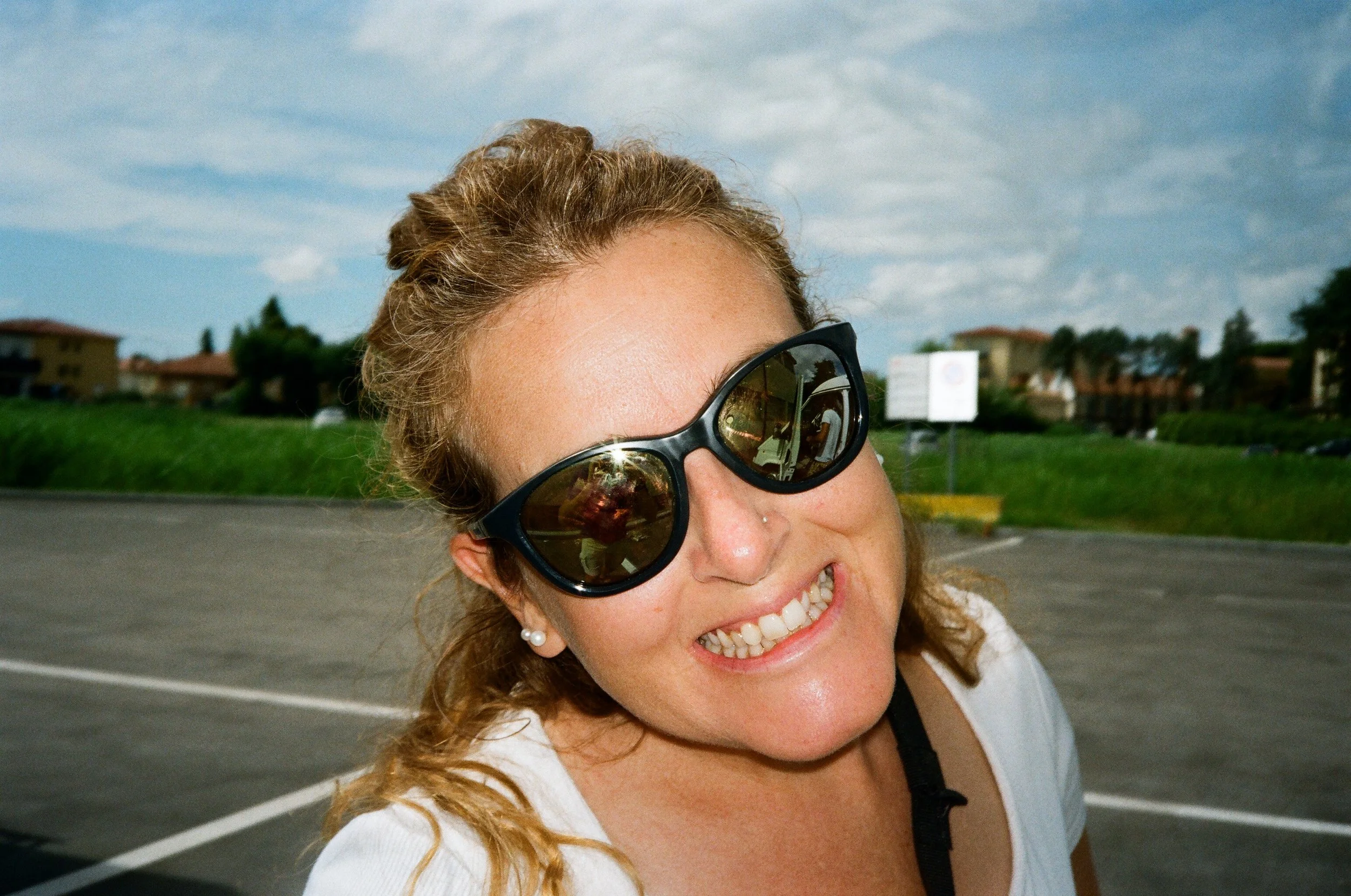 Donna sorridente con occhiali da sole in un parcheggio all'aperto.