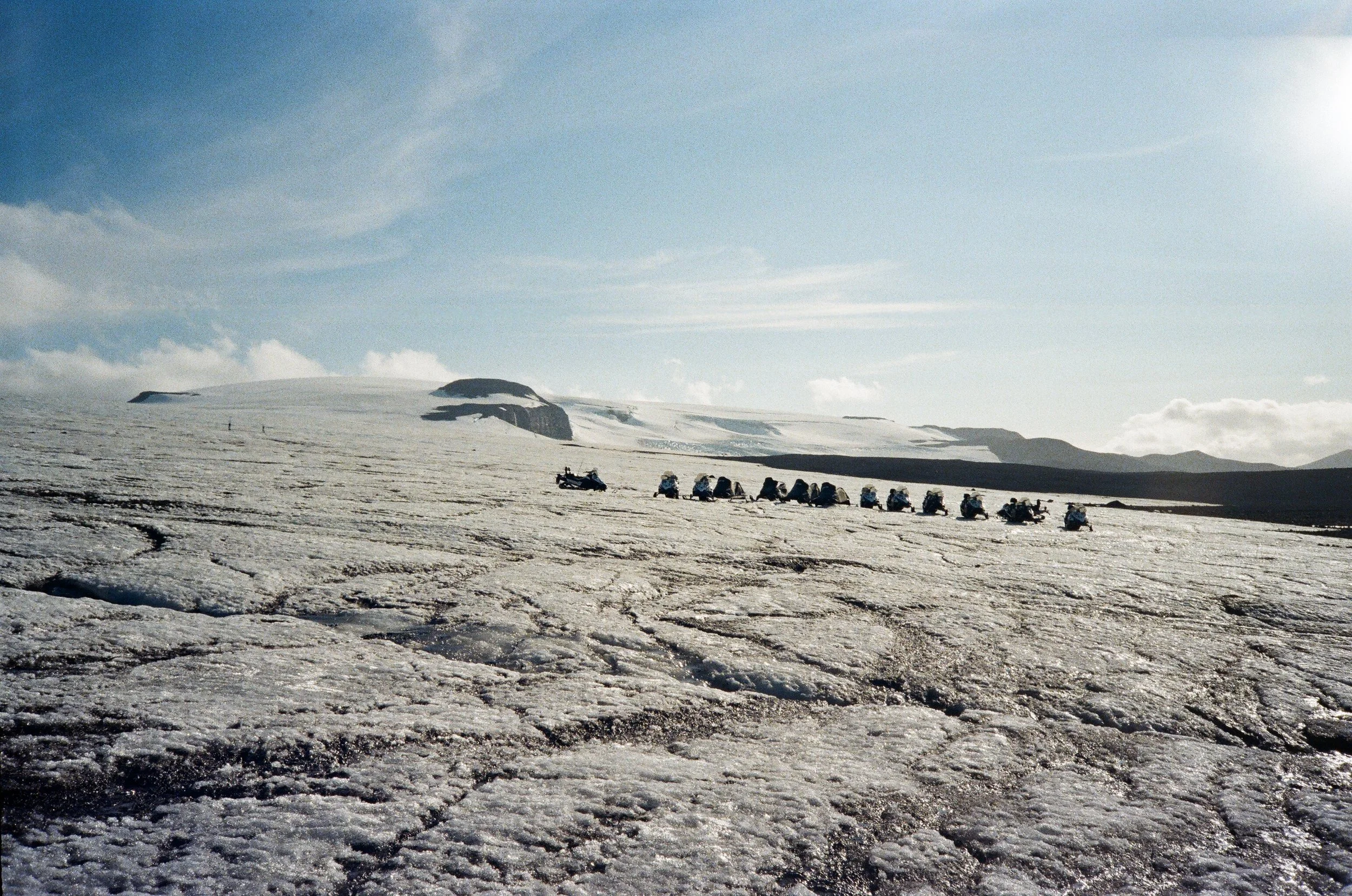 Gruppo di motociclisti in viaggio su un paesaggio ghiacciato con cielo azzurro e cumuli di neve sullo sfondo.