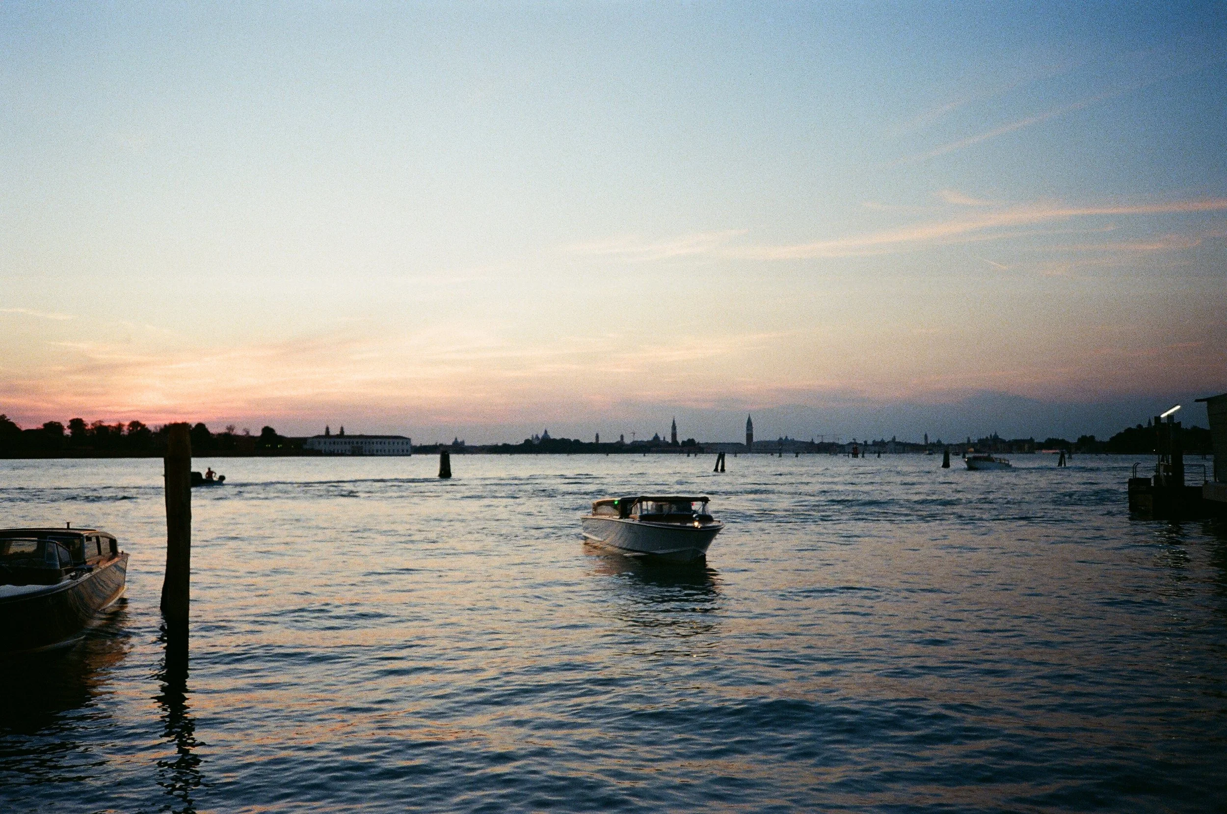 Vista del fiume con barche al tramonto, con edifici e torri sullo sfondo a Venezia