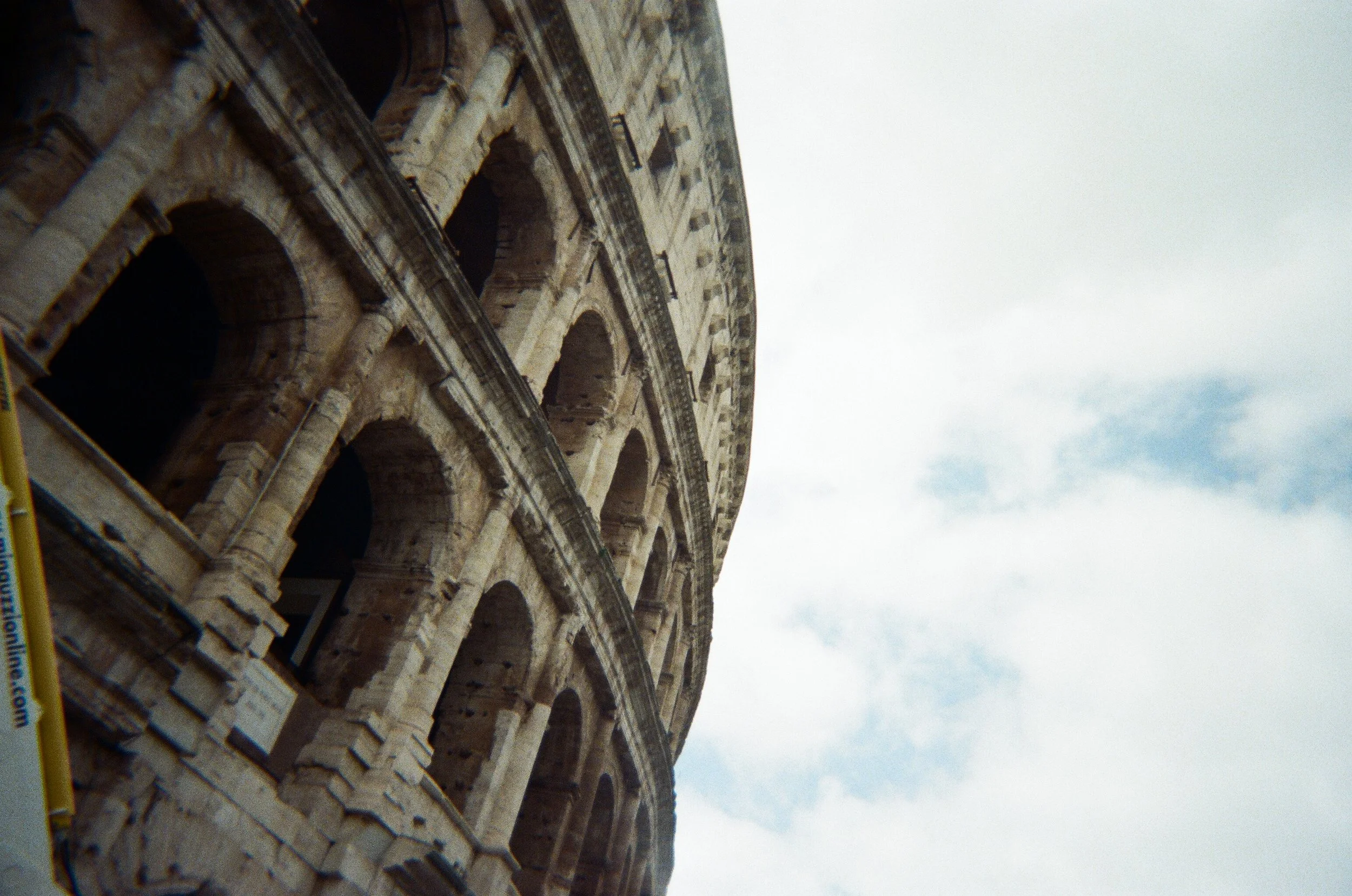 Vista laterale del Colosseo di Roma con cielo nuvoloso sullo sfondo.