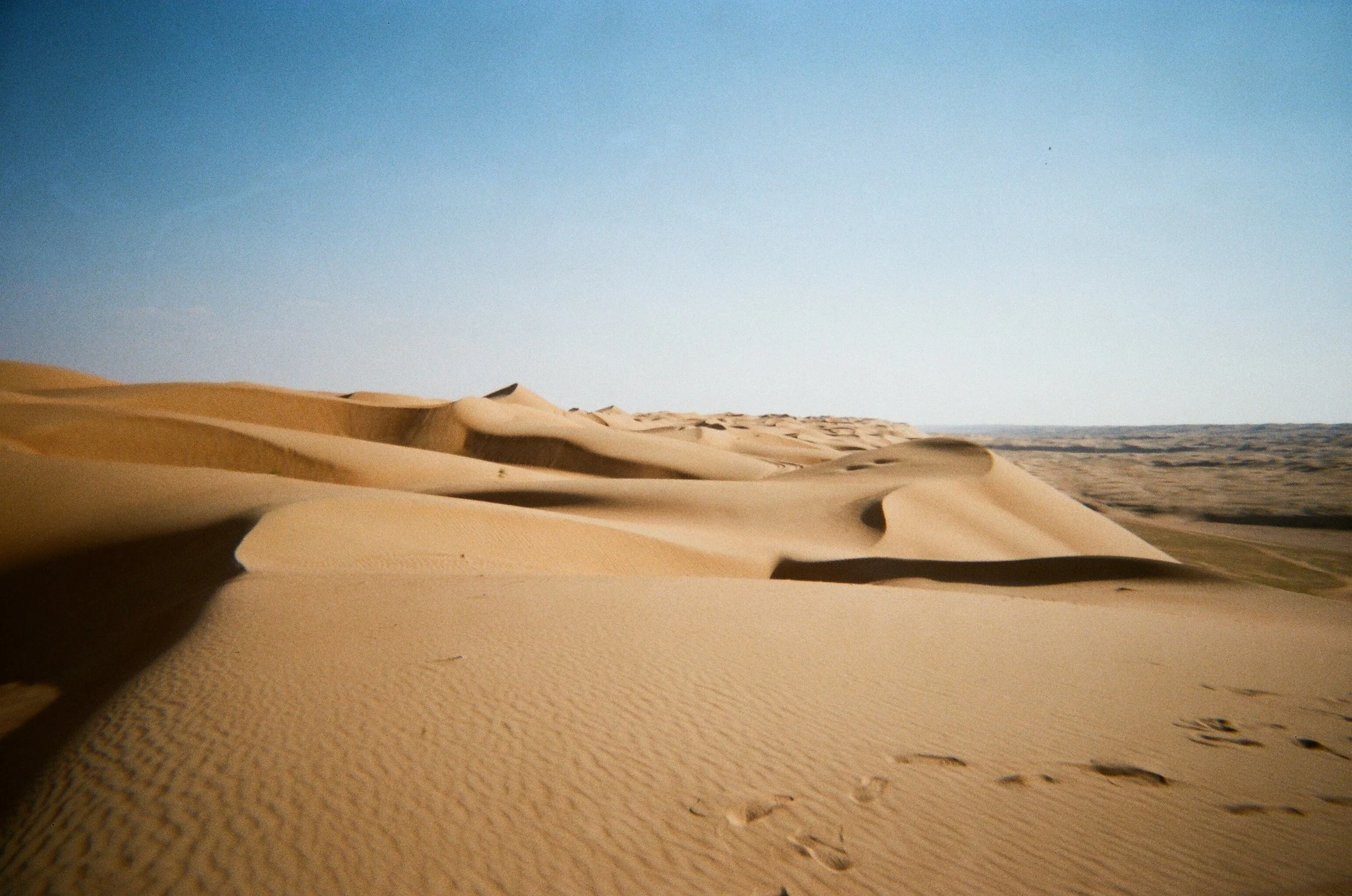 Dune di sabbia nel deserto sotto un cielo chiaro e azzurro.